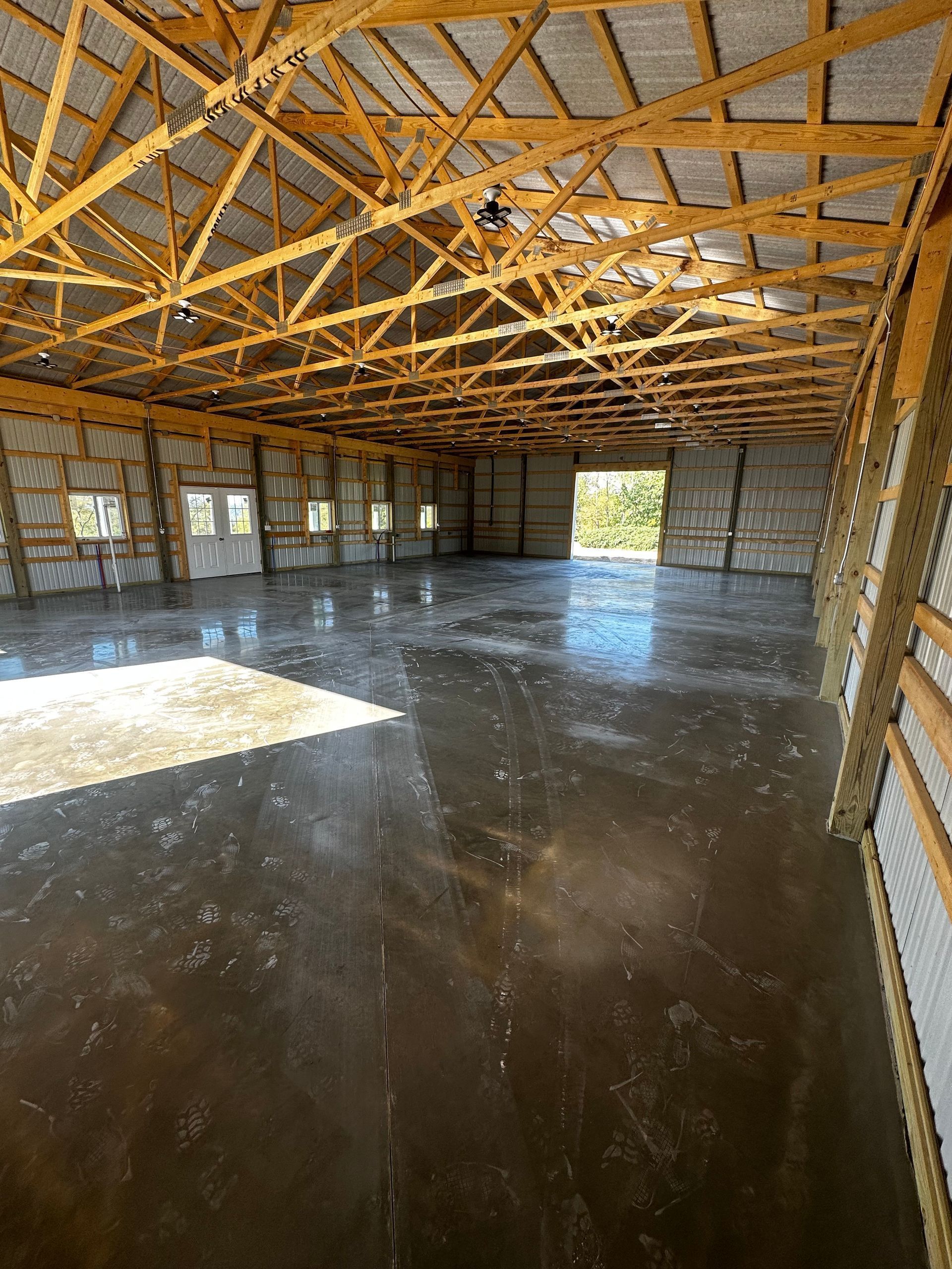 Empty unfinished interior with exposed wooden trusses and a concrete floor, lit by daylight through open walls