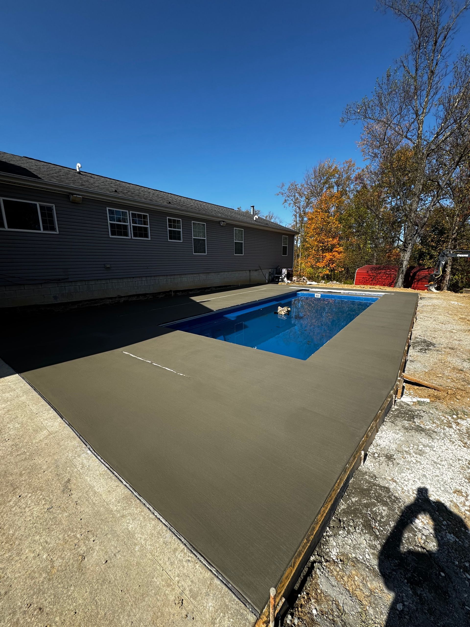 Backyard patio with a rectangular blue pool beside a gray house on a sunny day