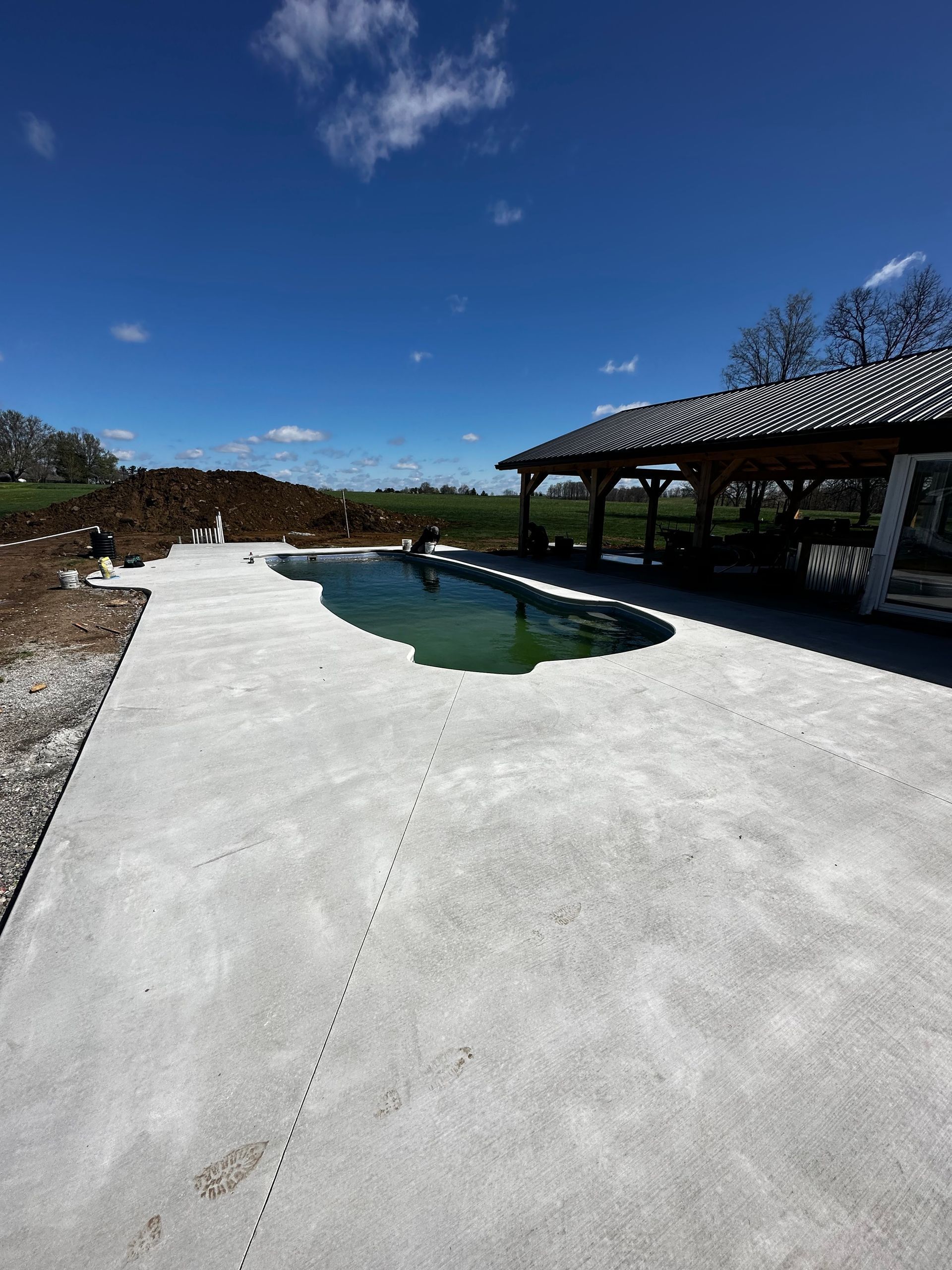Backyard pool with white deck, blue water, and covered patio under a clear sky