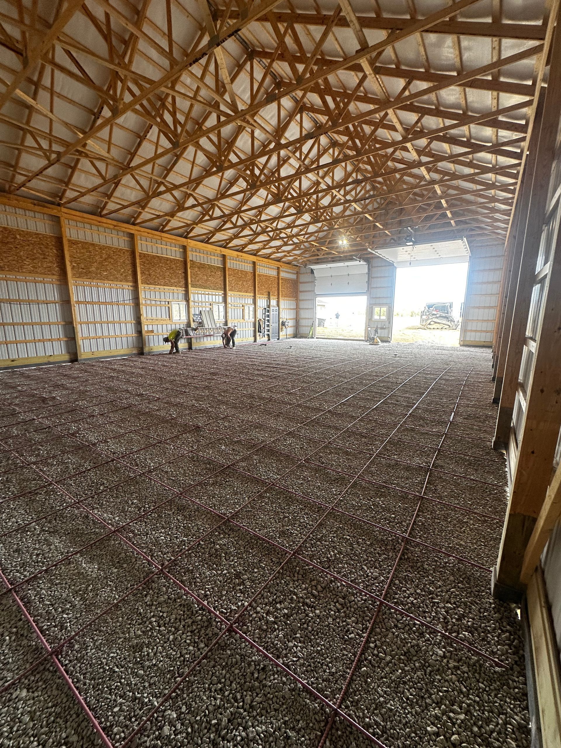 Spacious barn interior with a gravel floor, wooden trusses, and bright open doorways at the far end