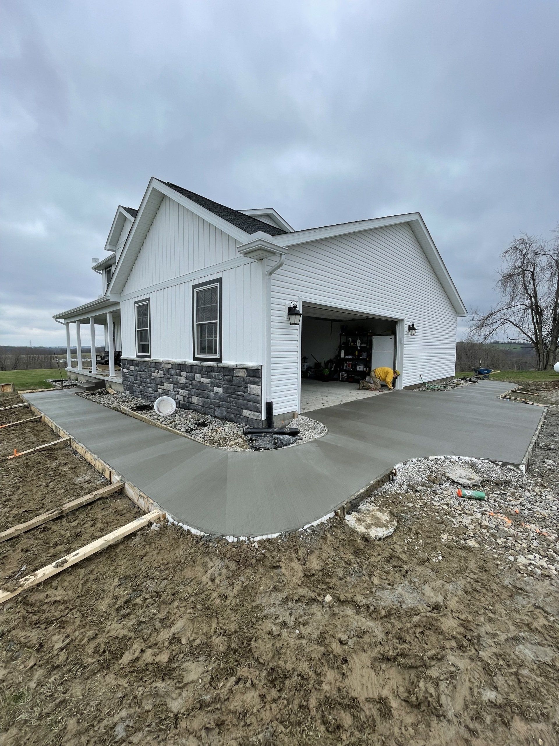 White house under construction with attached garage, concrete driveway, and overcast sky
