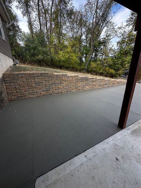 Patio with smooth gray concrete beside a brick retaining wall and wooded slope
