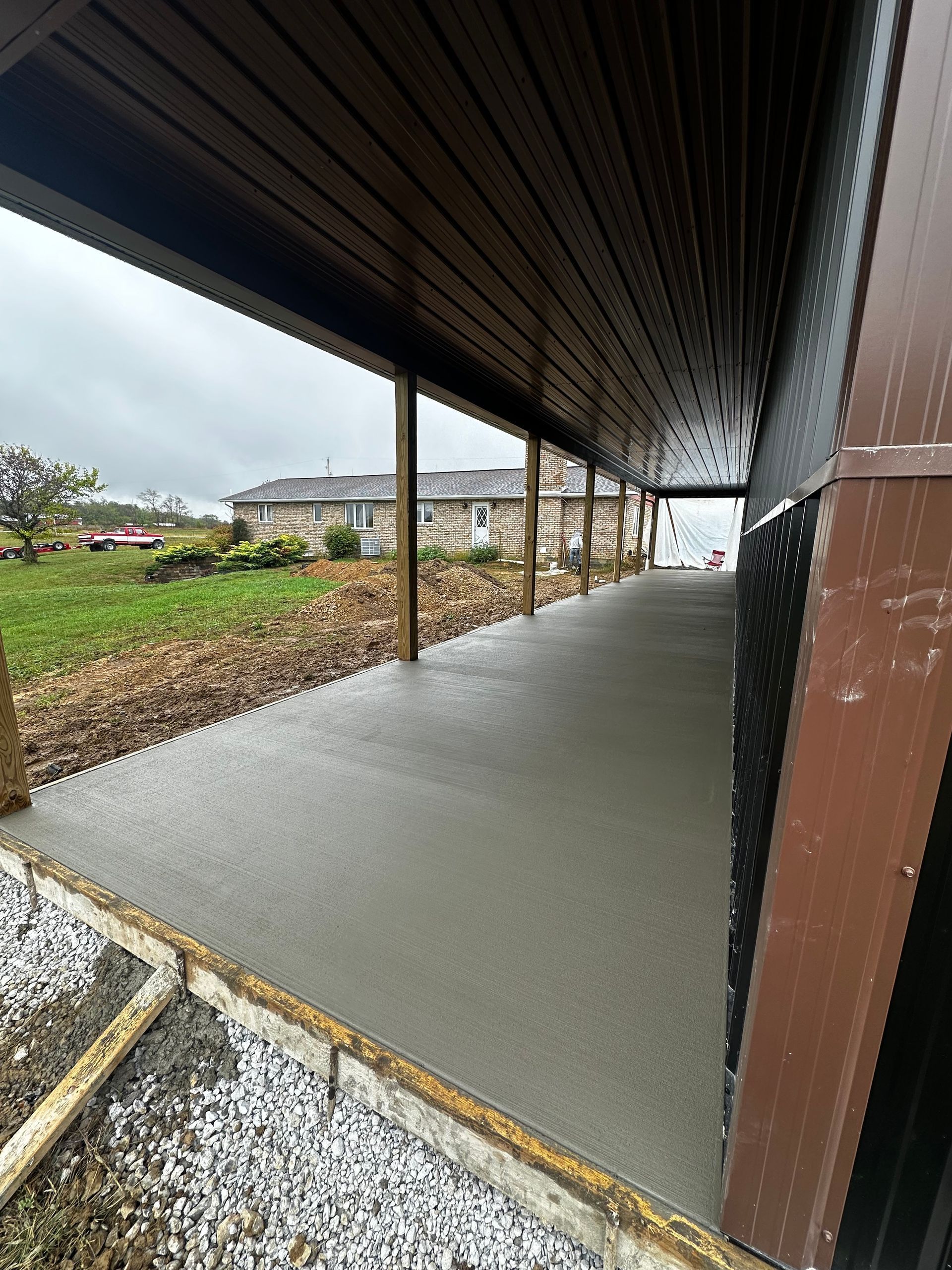 Covered outdoor walkway with fresh concrete floor and open views of a yard and neighboring houses.
