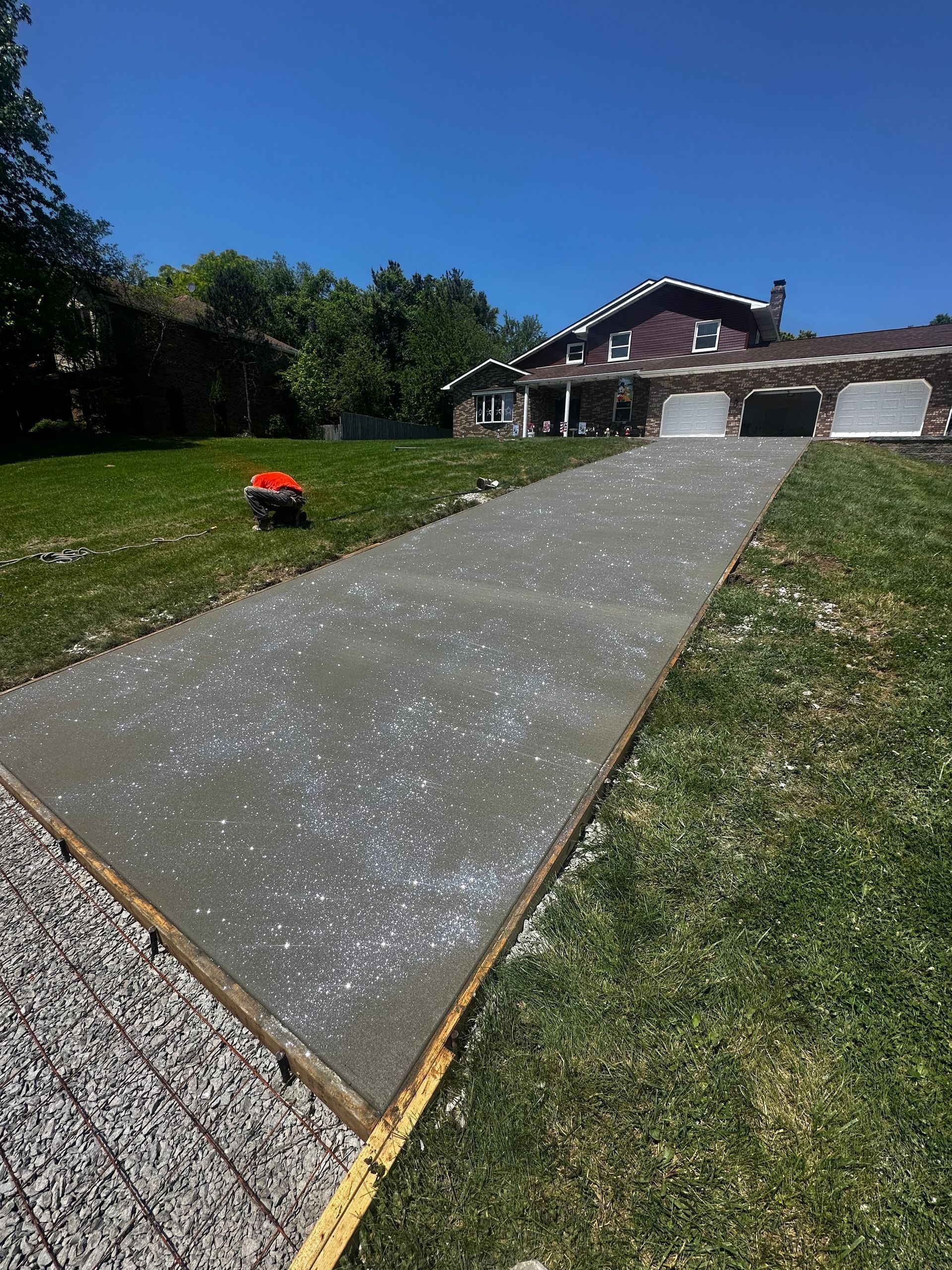 Concrete driveway leading to a house with a red lawn mower on the grass and blue sky above