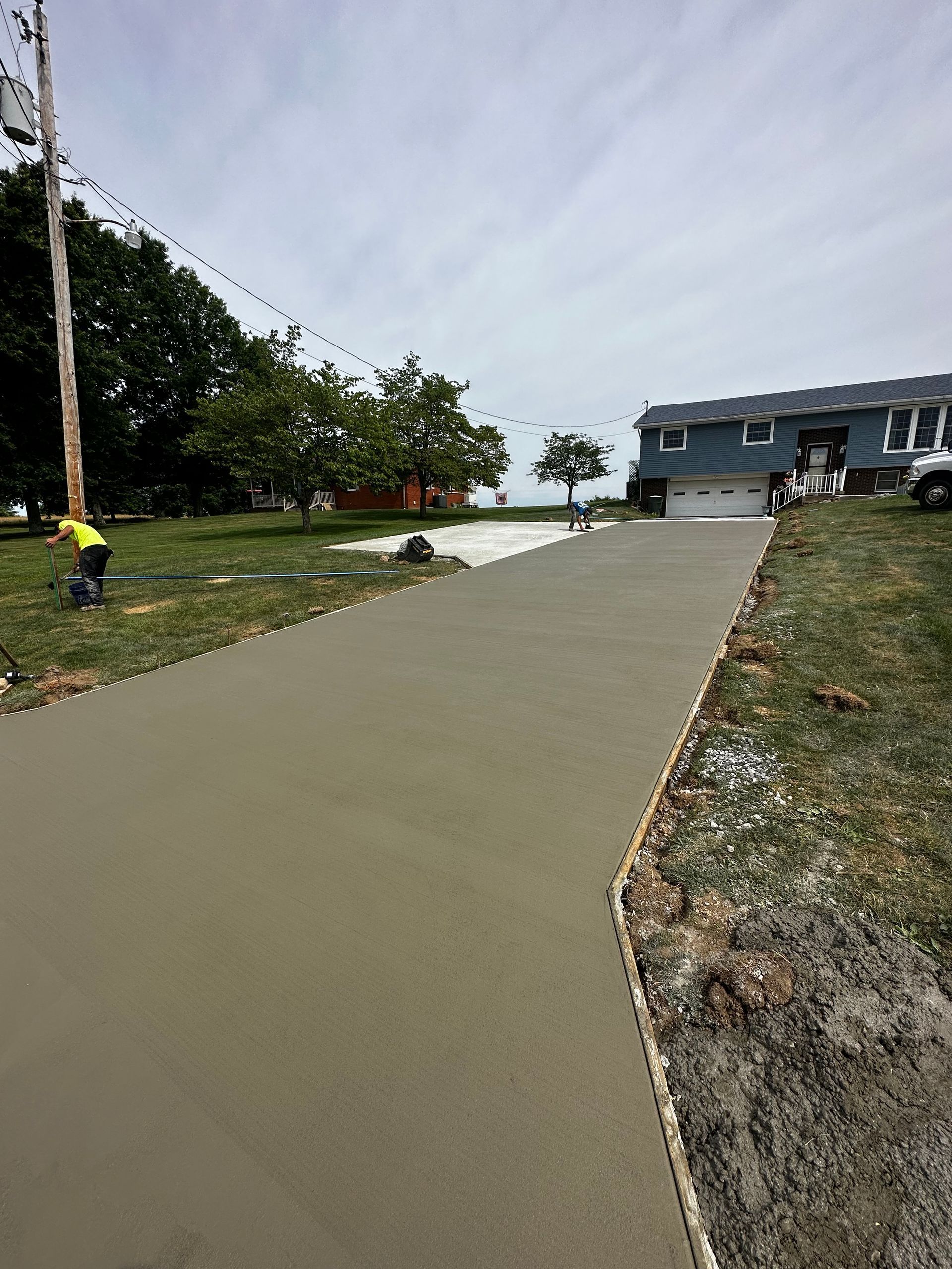 Curved concrete walkway leading to a building, with a worker on the left and trees along the side.