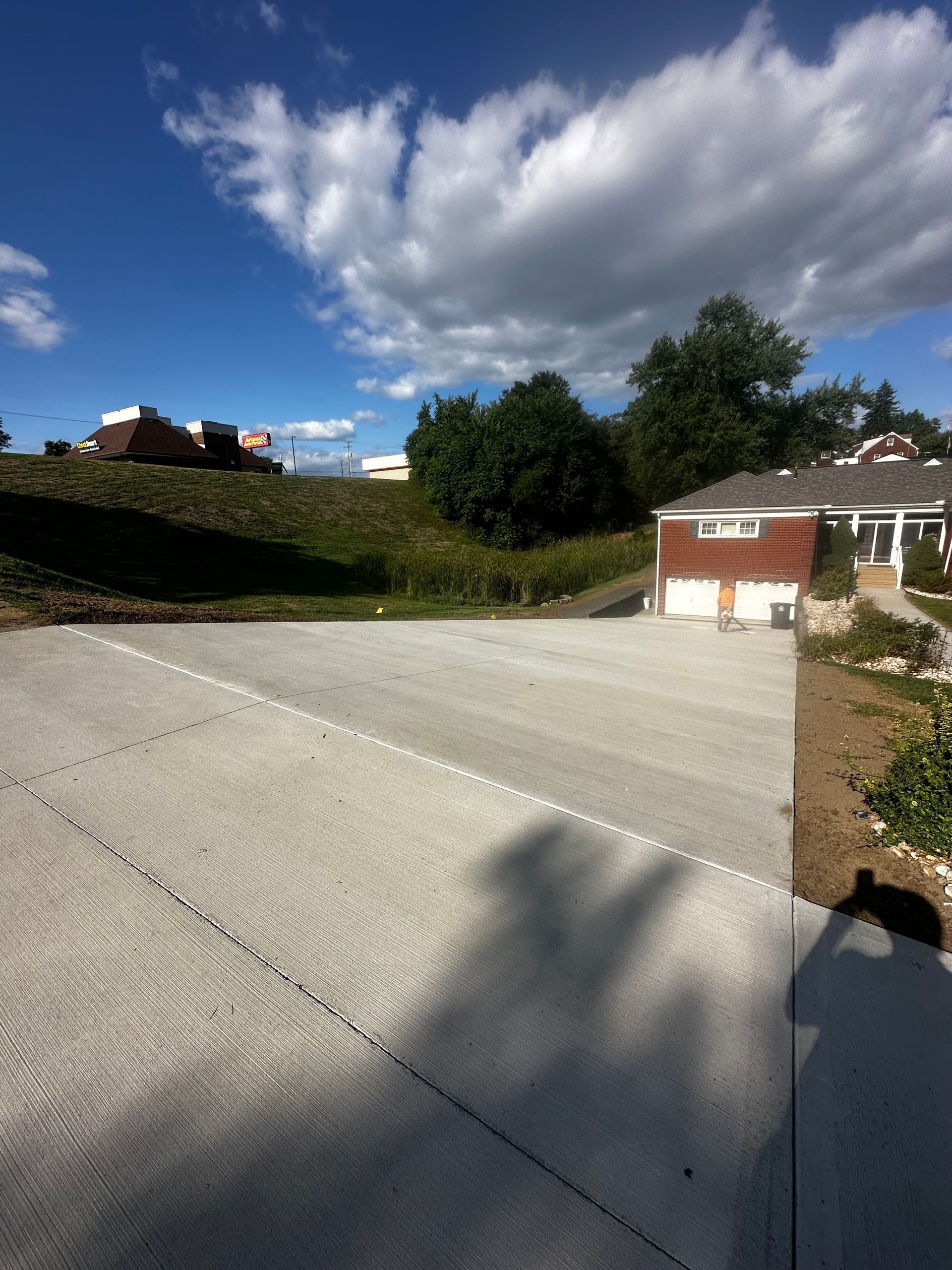 Concrete driveway under a blue sky with large clouds, trees, and houses in a suburban neighborhood