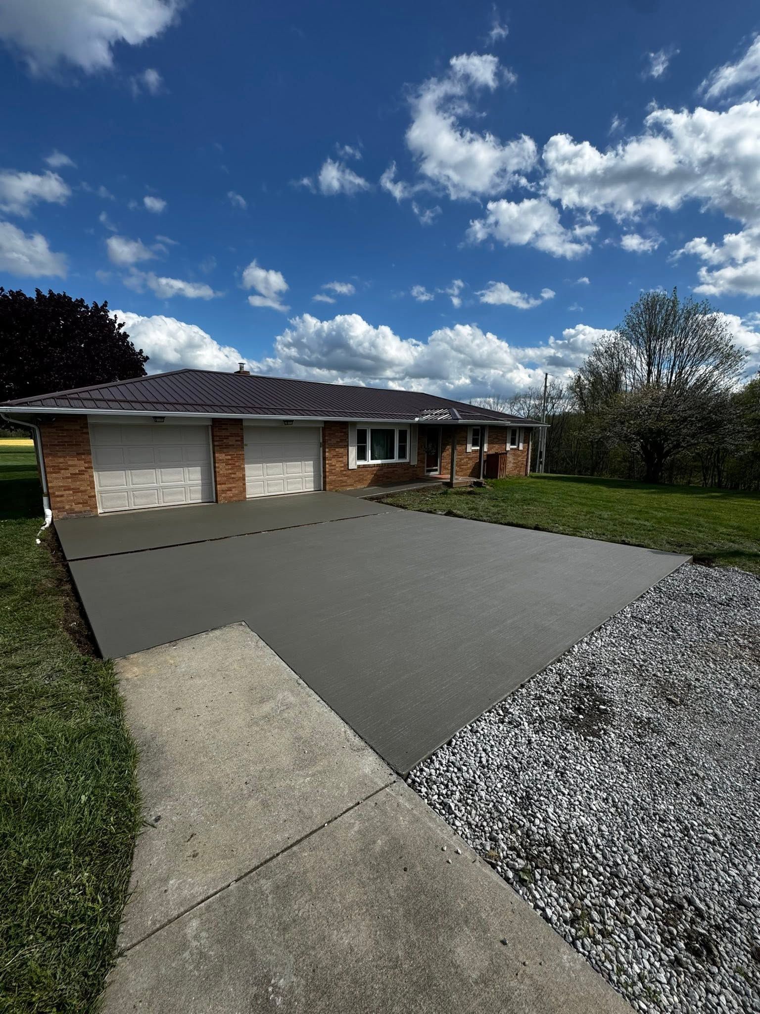 Suburban house with a wide driveway, gravel border, and partly cloudy blue sky
