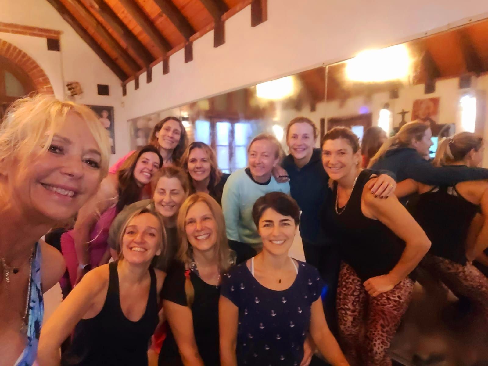 Grupo de personas sonriendo para una selfi en una sala interior con vigas de madera e iluminación cálida