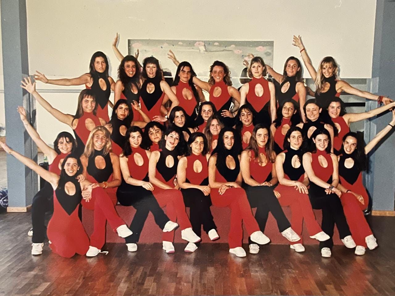 Un equipo de baile posa con trajes rojos, formando una composición simétrica en interiores.