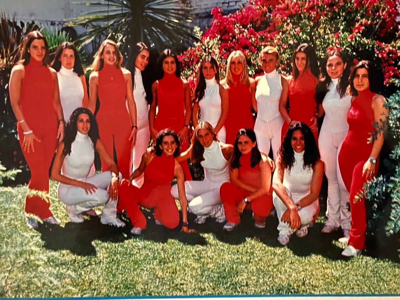 Grupo de personas posando al aire libre con conjuntos a juego en rojo y blanco, en un césped soleado