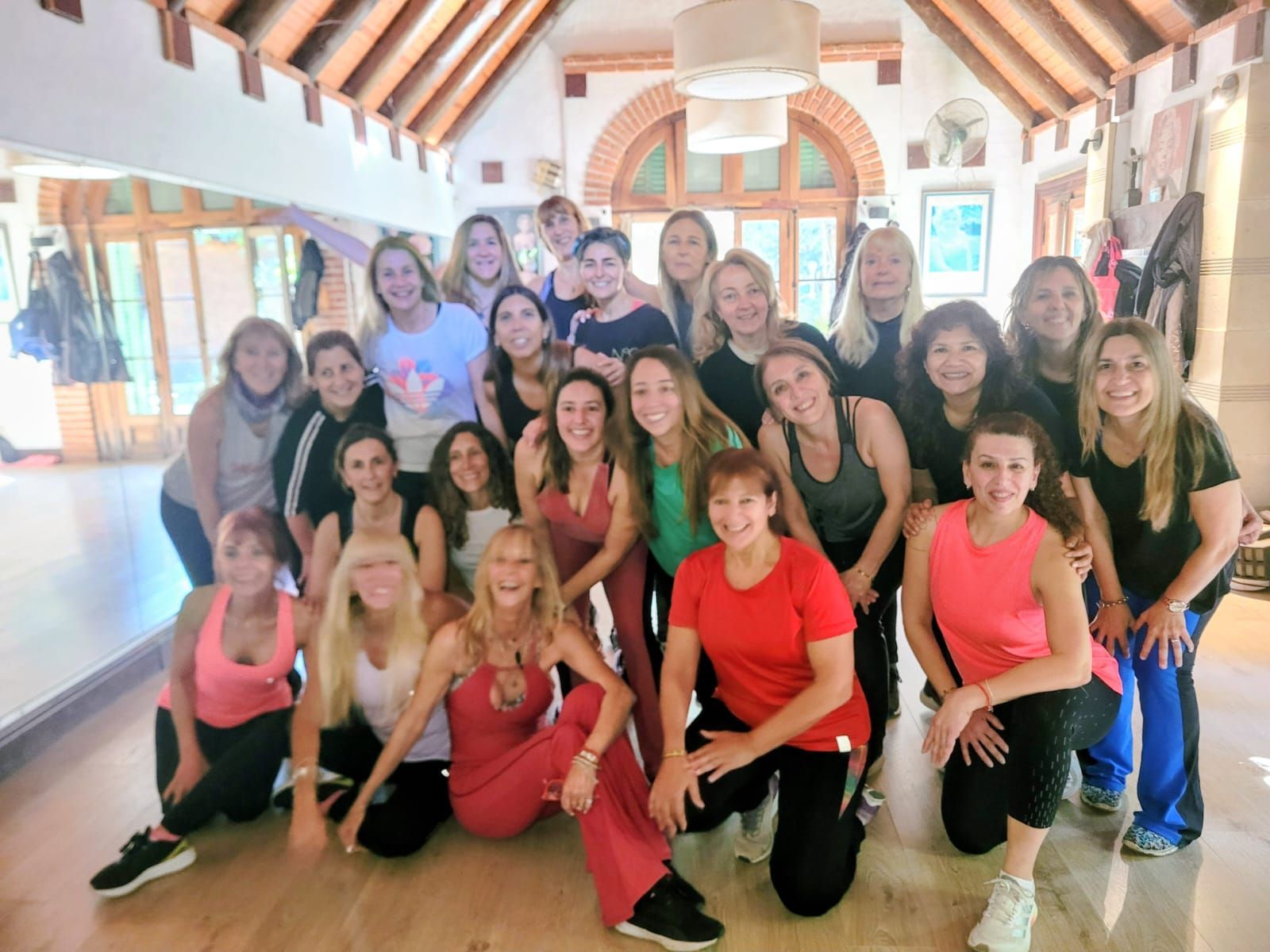 Grupo de personas posando en un estudio luminoso, muchas con atuendos rojos y negros, sonriendo para una foto de equipo