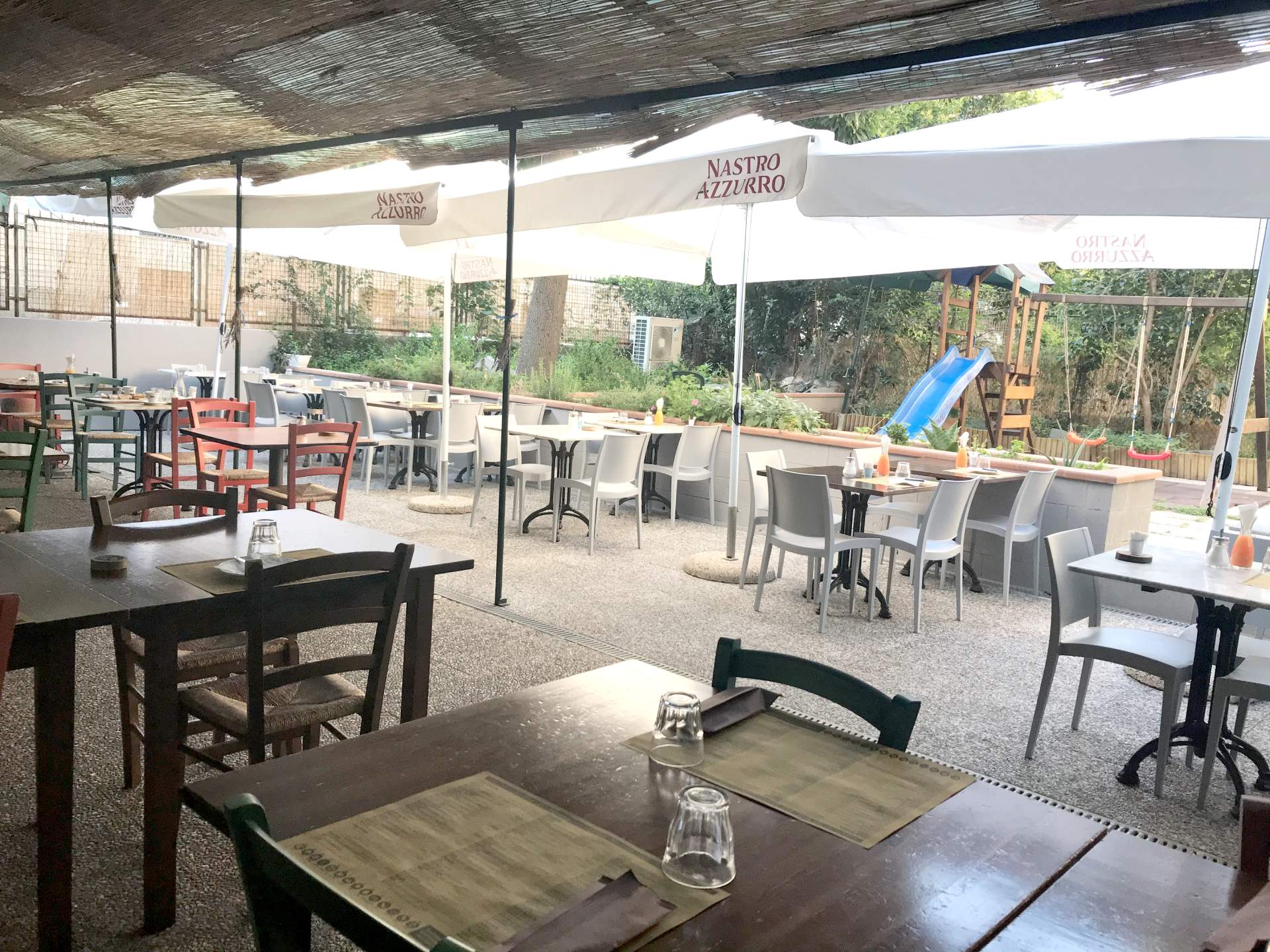 Un ristorante con tavoli e sedie sotto gli ombrelloni e un parco giochi sullo sfondo