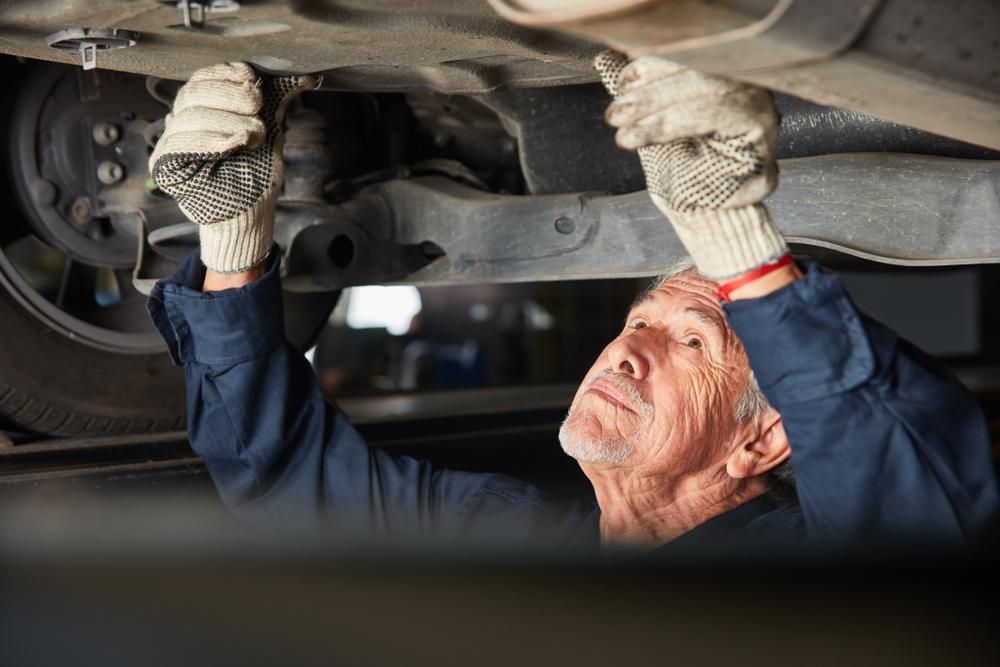 An Older Man Is Working Under A Car In A Garage — Platinum Paint & Panel Southport In Southport, QLD