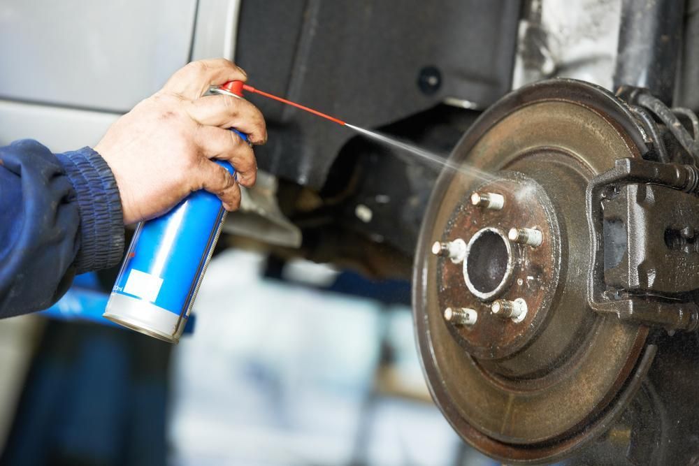 A Person Is Spraying A Can Of Lubricant On A Brake Disc — Platinum Paint & Panel Southport In Southport, QLD