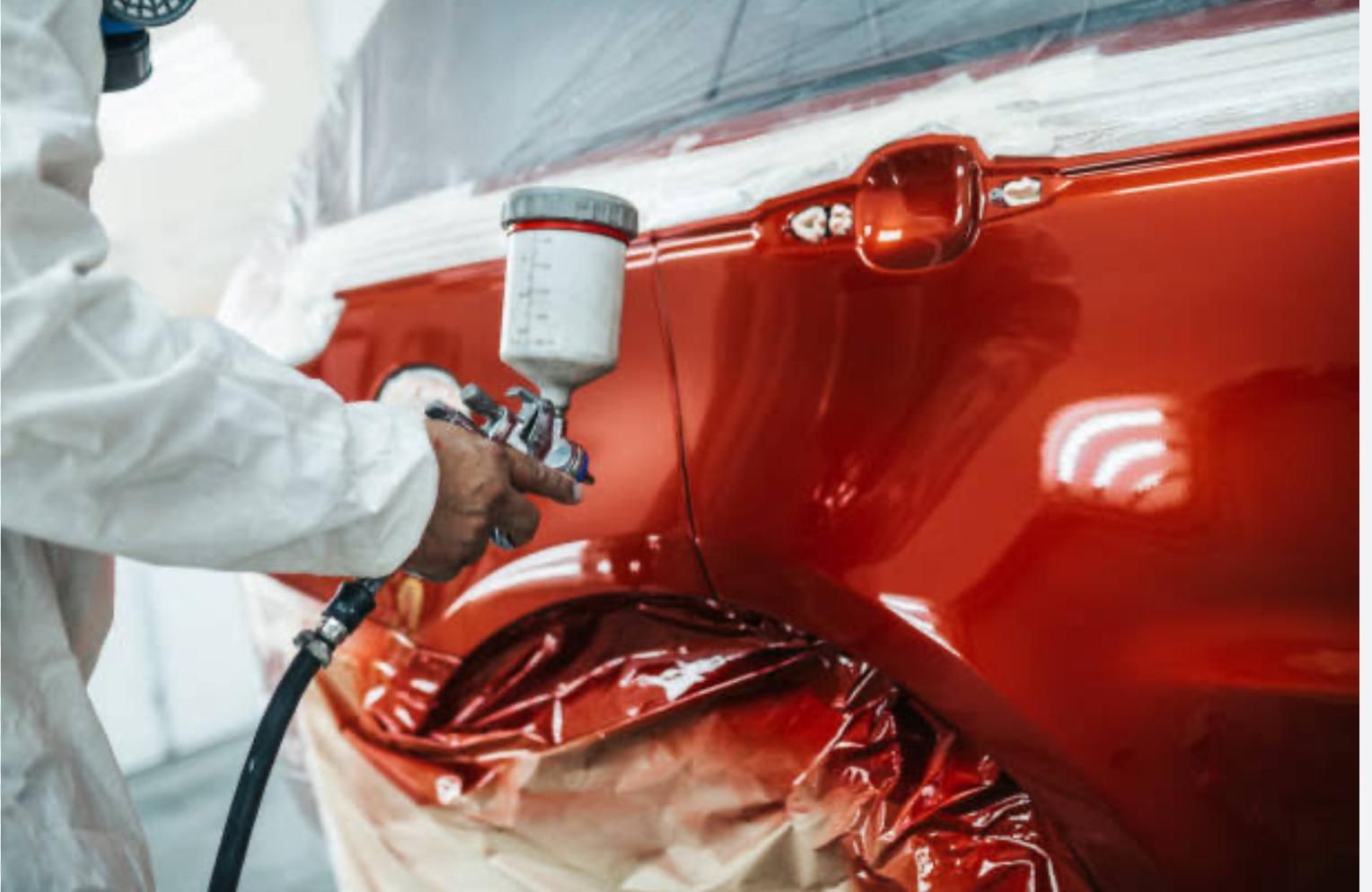 A Man Is Spray Painting A Red Car In A Garage — Platinum Paint & Panel Southport In Southport, QLD