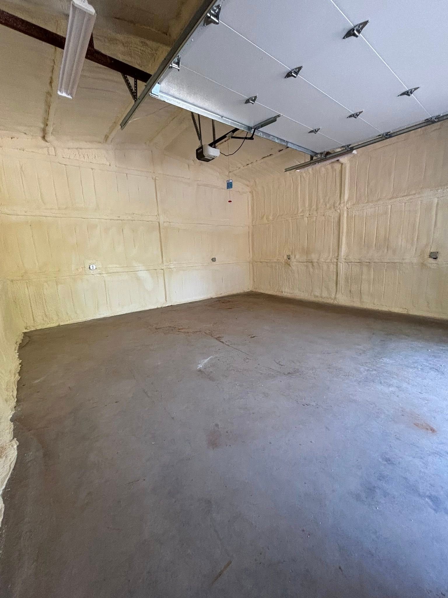 Empty unfinished garage with unfinished walls, concrete floor, and exposed ceiling insulation.