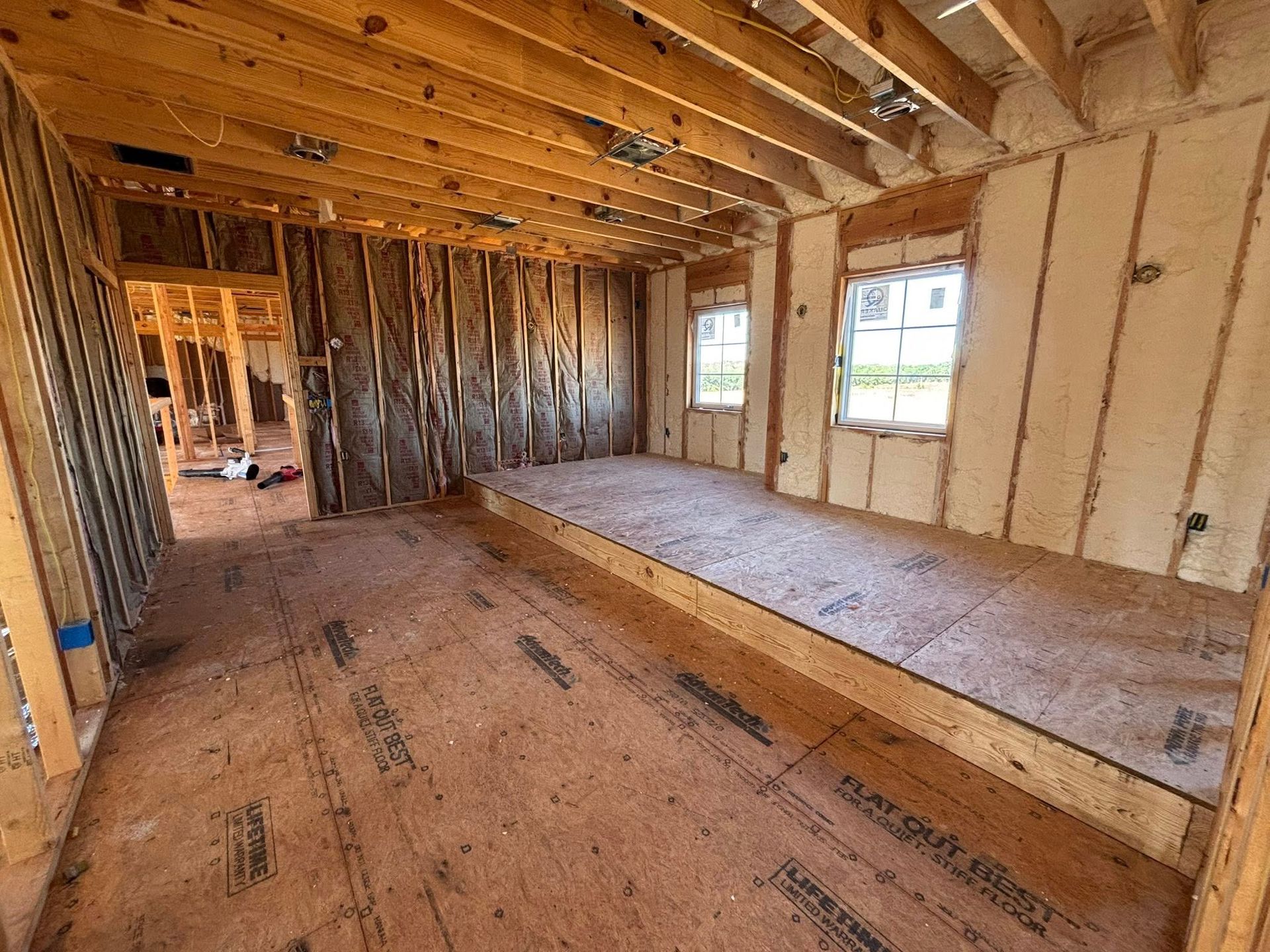 Unfinished wooden room with exposed beams, insulation, and a raised platform by the windows