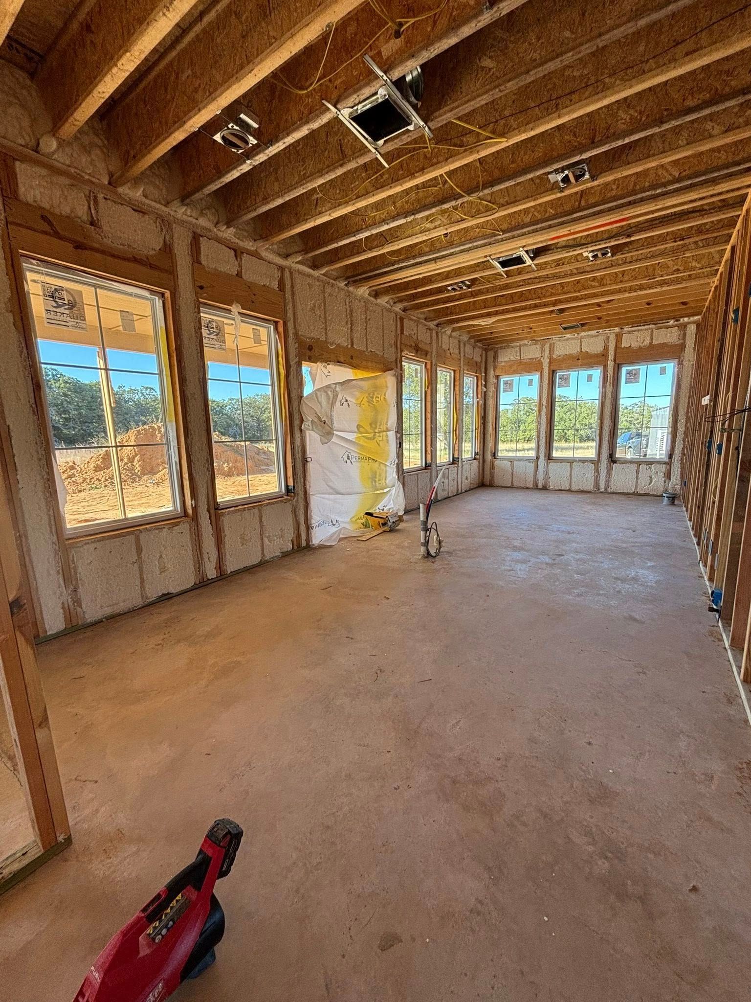Unfinished room framed with exposed wood, windows, and bare subfloor under construction.