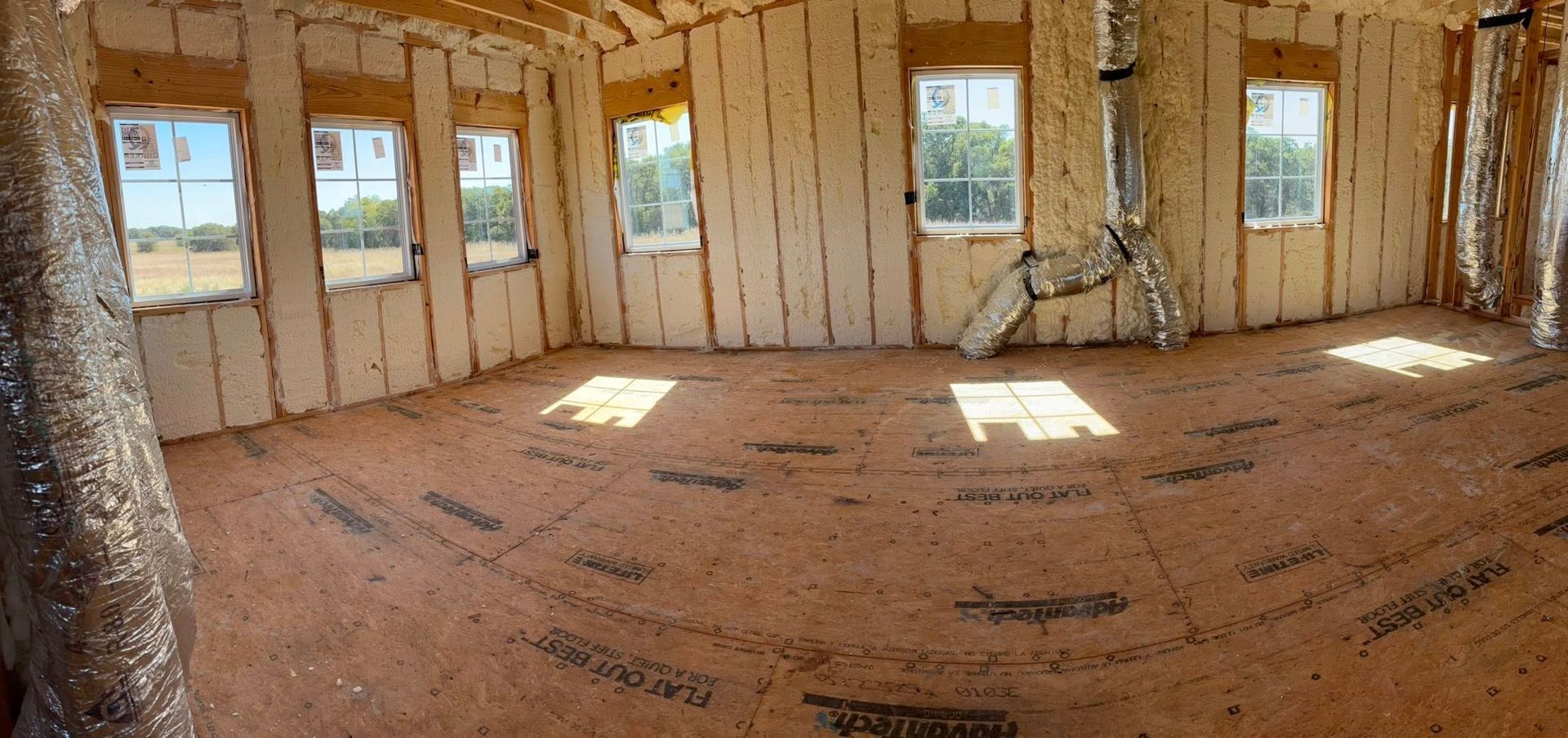 Unfinished room with exposed wood framing, large windows, and sunlight on the dusty floor