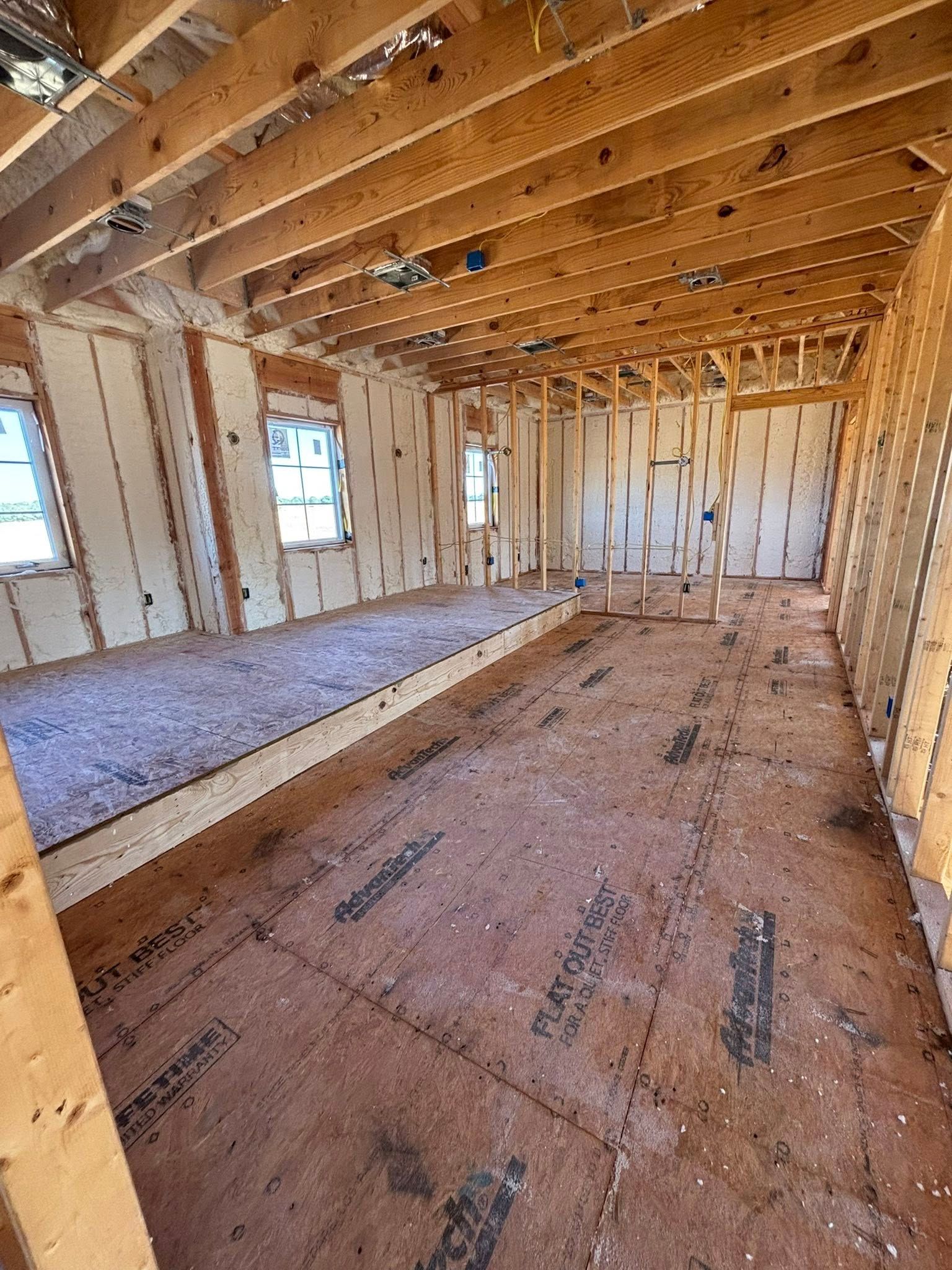 Unfinished room under construction with exposed wood framing, floor joists, and insulation along the walls