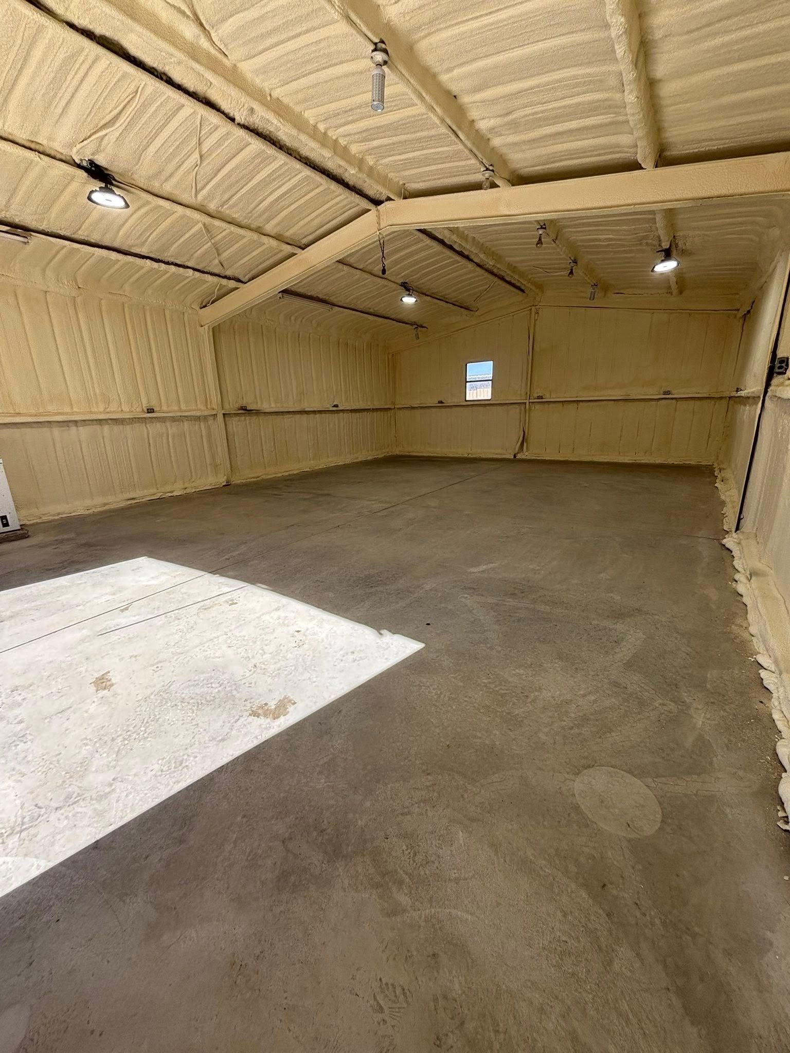 Empty beige insulated garage with concrete floor and a small window