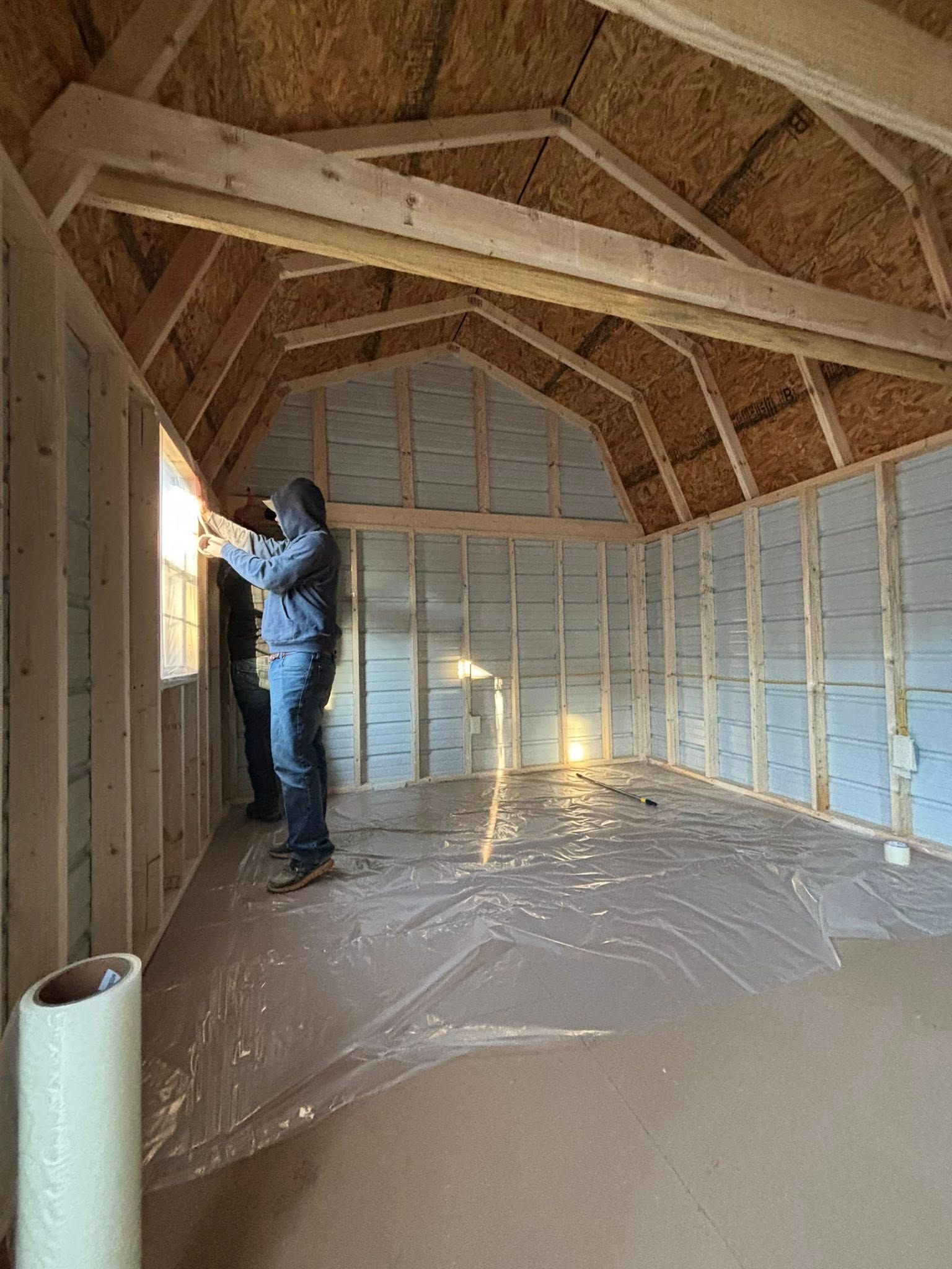 Worker installing insulation inside an unfinished attic with exposed wooden framing.
