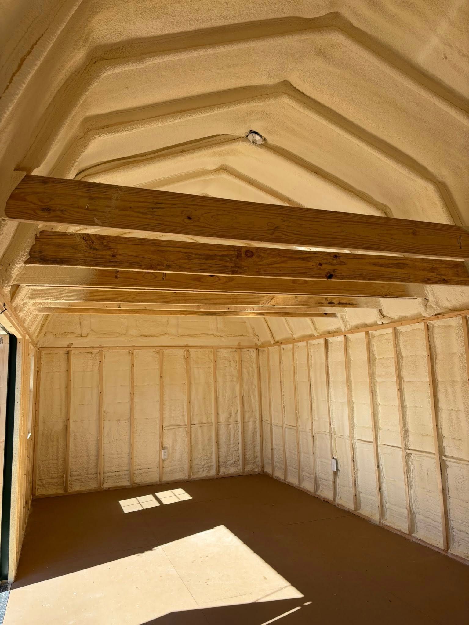 Empty insulated shed interior with exposed beams and sunlight on the floor