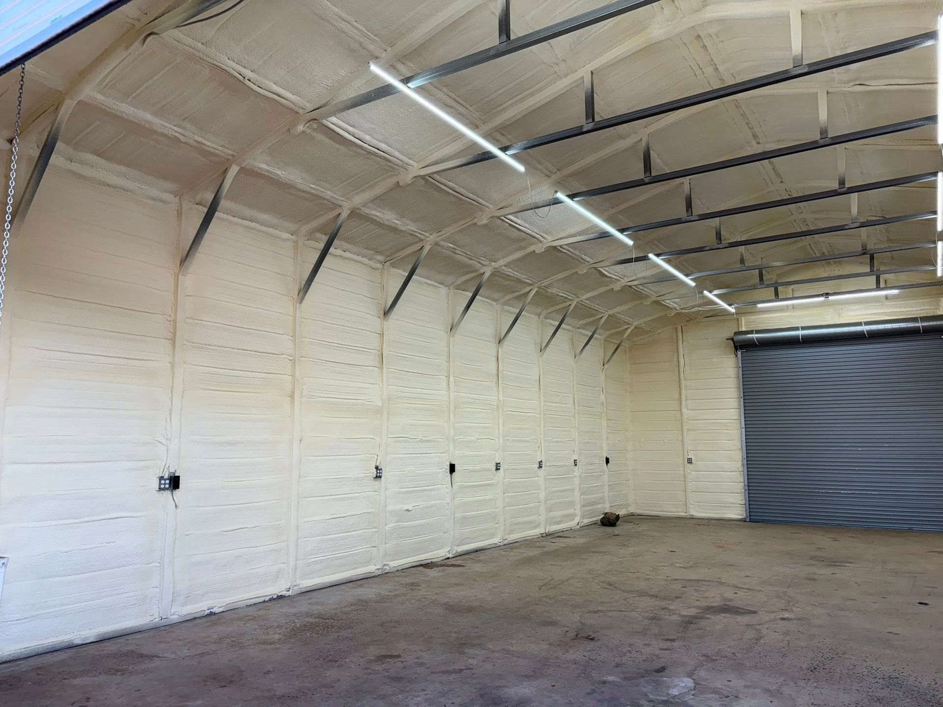 Empty warehouse interior with white insulated walls, curved ceiling, and a closed gray roll-up door