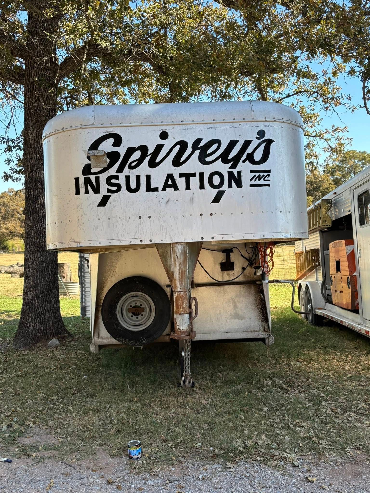 Spivey’s Insulation trailer in a grassy yard, with trees and a white tank on a truck bed
