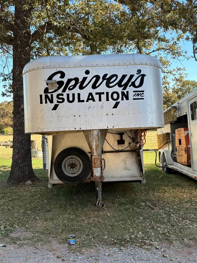 Spivey’s Insulation trailer parked on grass beneath trees, with a truck wheel visible underneath