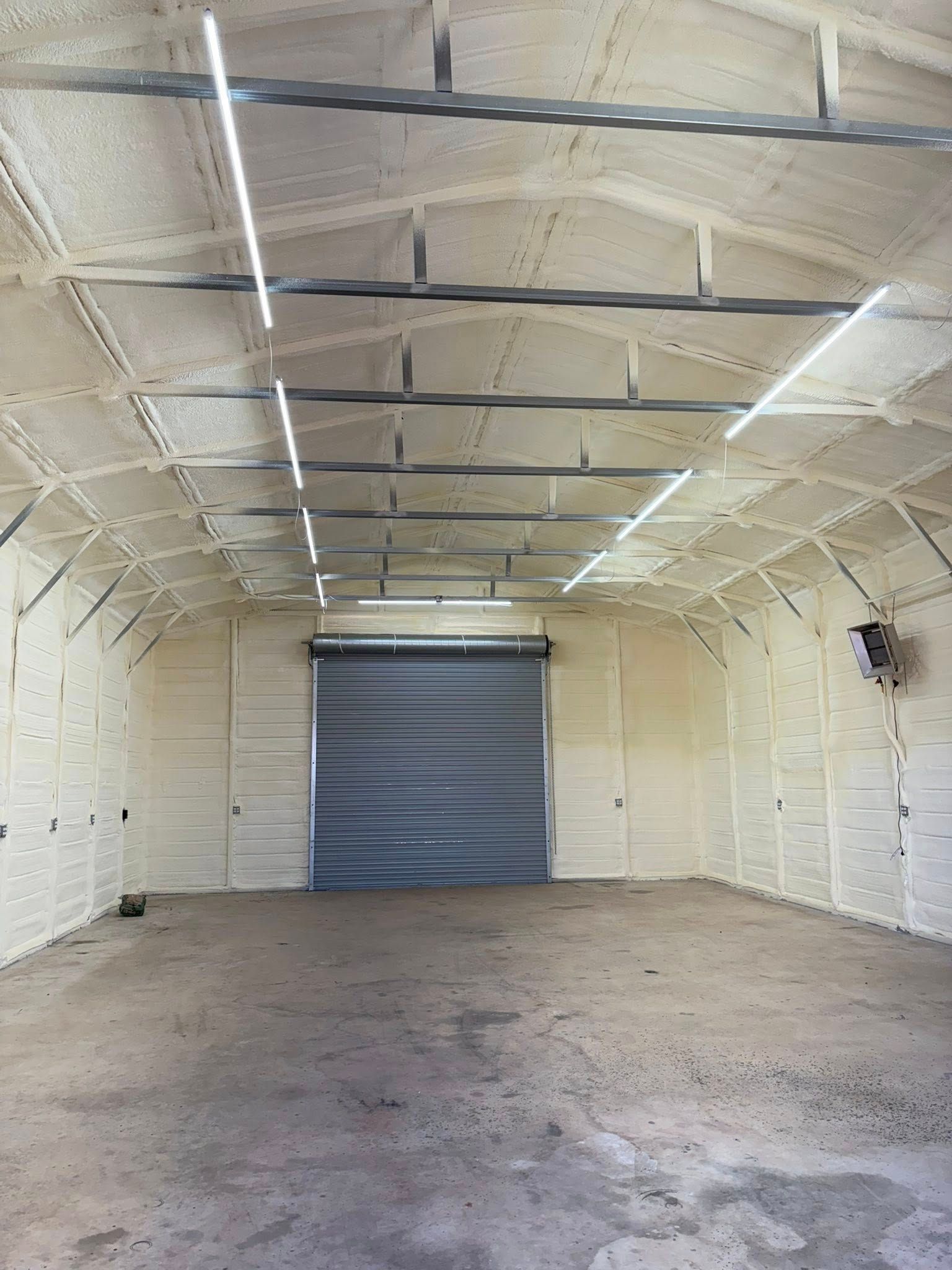 Empty white warehouse interior with a gray roll-up door and concrete floor