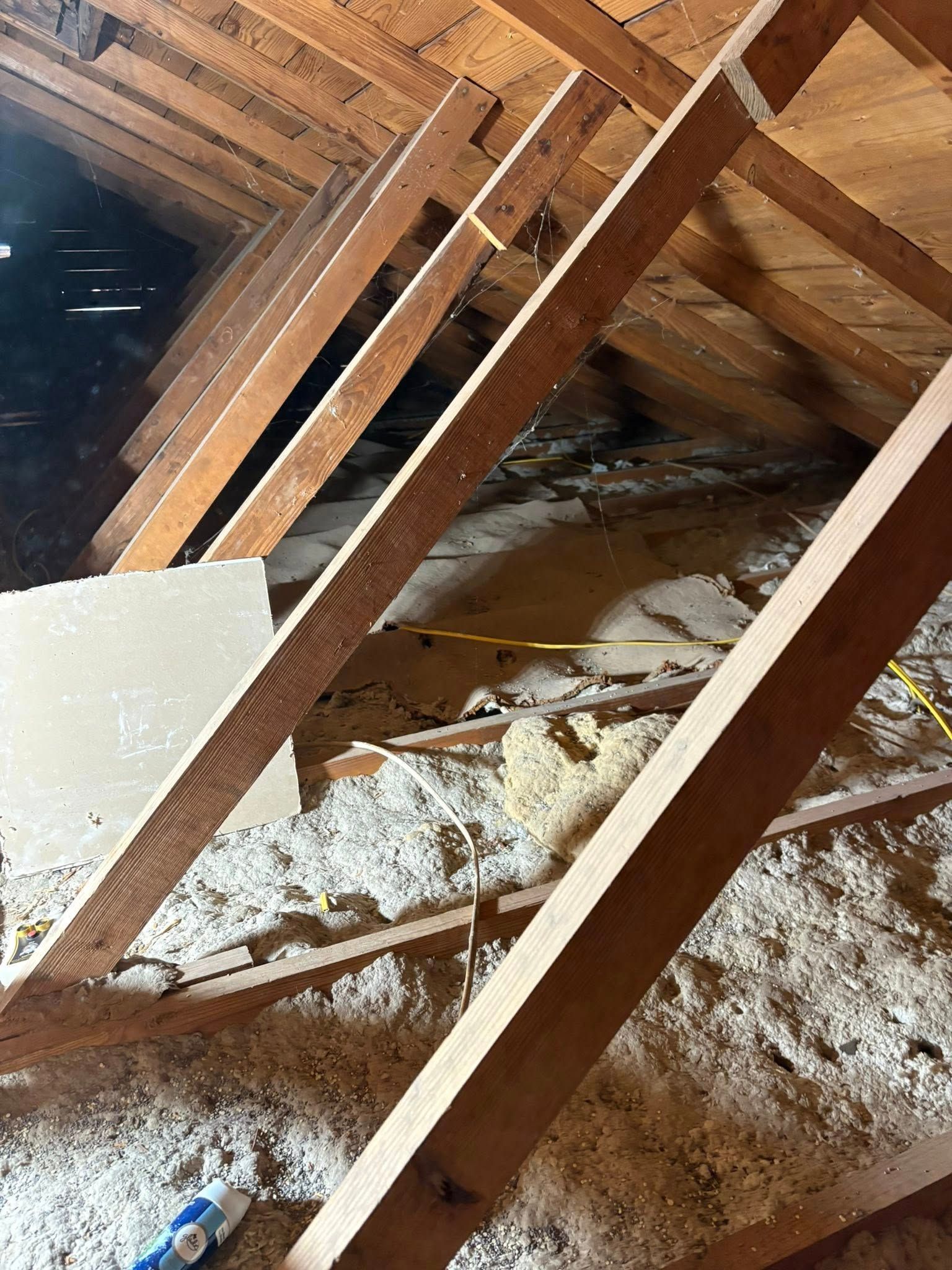 Attic with exposed wooden rafters, slanted beams, and scattered insulation on the floor