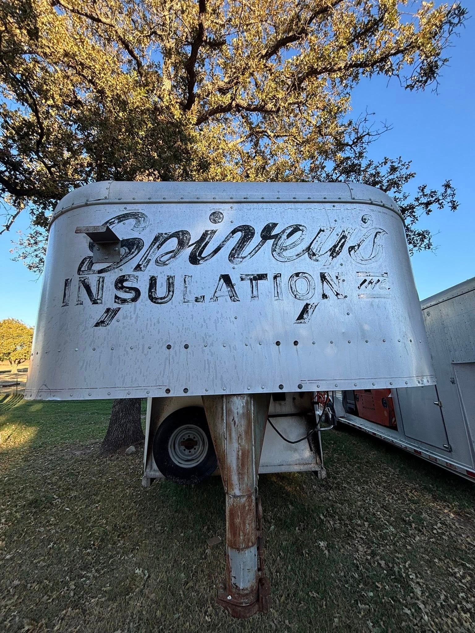 Weathered metal sign reading “Soda Insulation” in front of a trailer and autumn tree