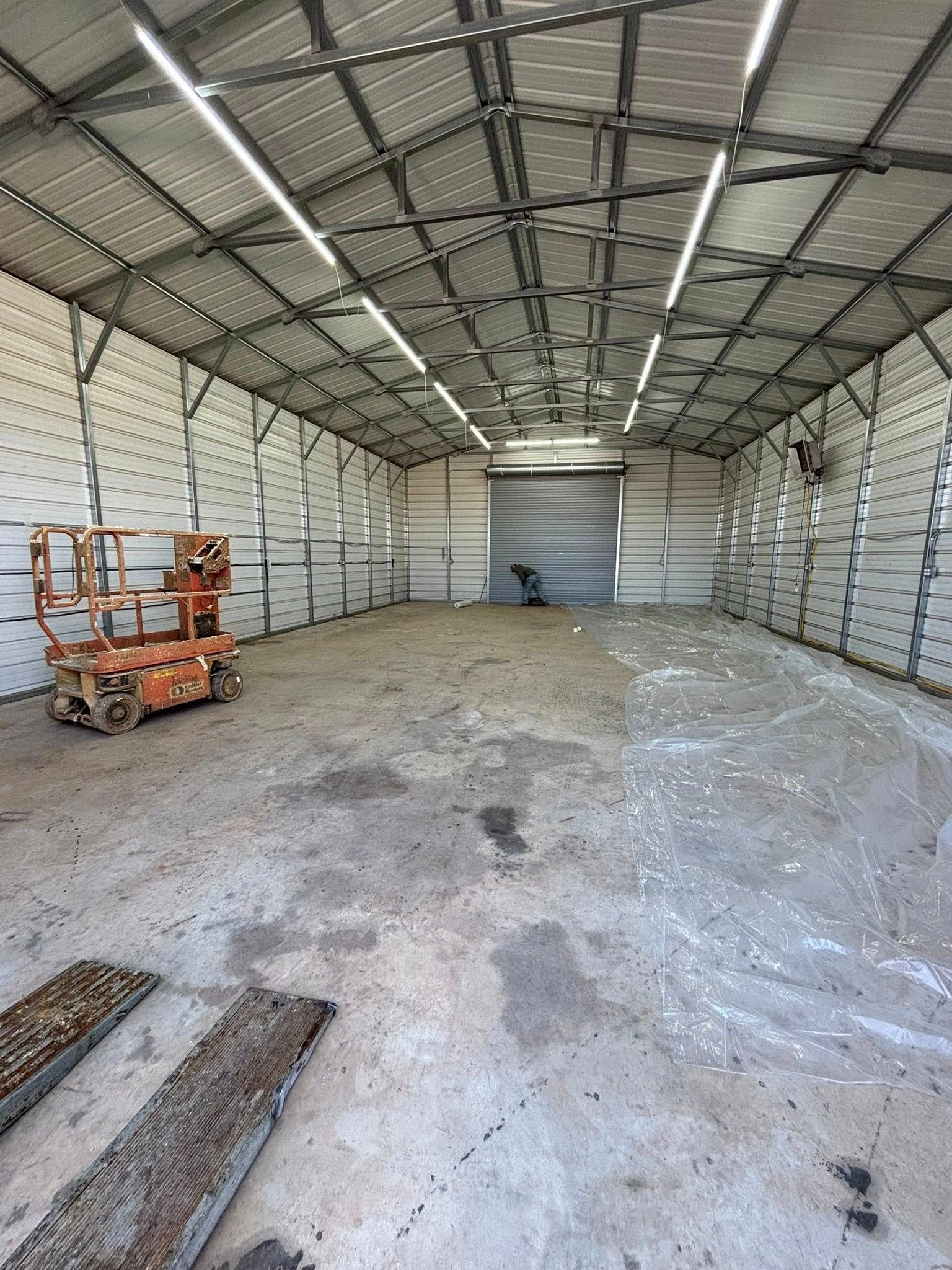 Empty industrial warehouse with gravel floor, metal walls, and orange scissor lift on the left