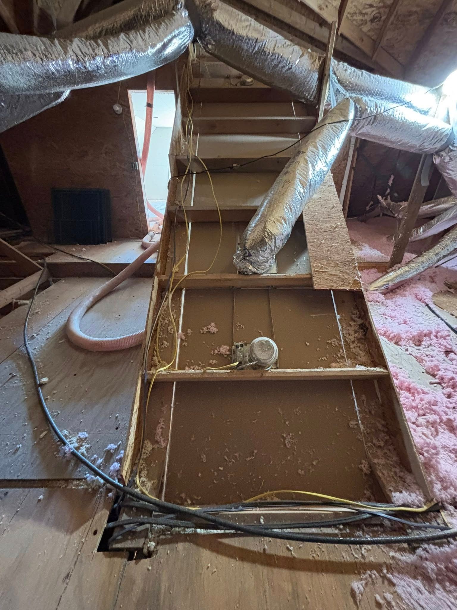 Collapsed attic insulation and debris with exposed ductwork and a bent ramp or panel on the floor.