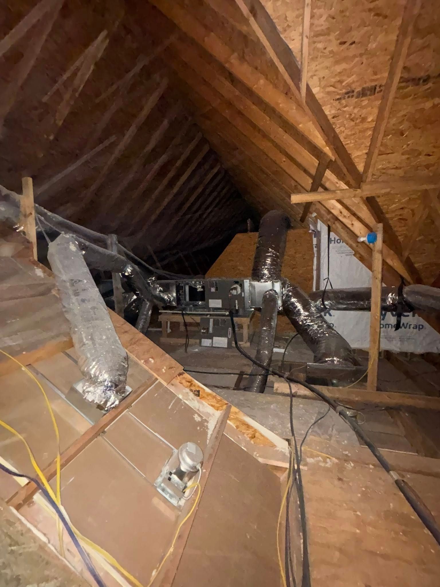 Attic interior with exposed wooden rafters, insulation, and HVAC ducts amid construction debris