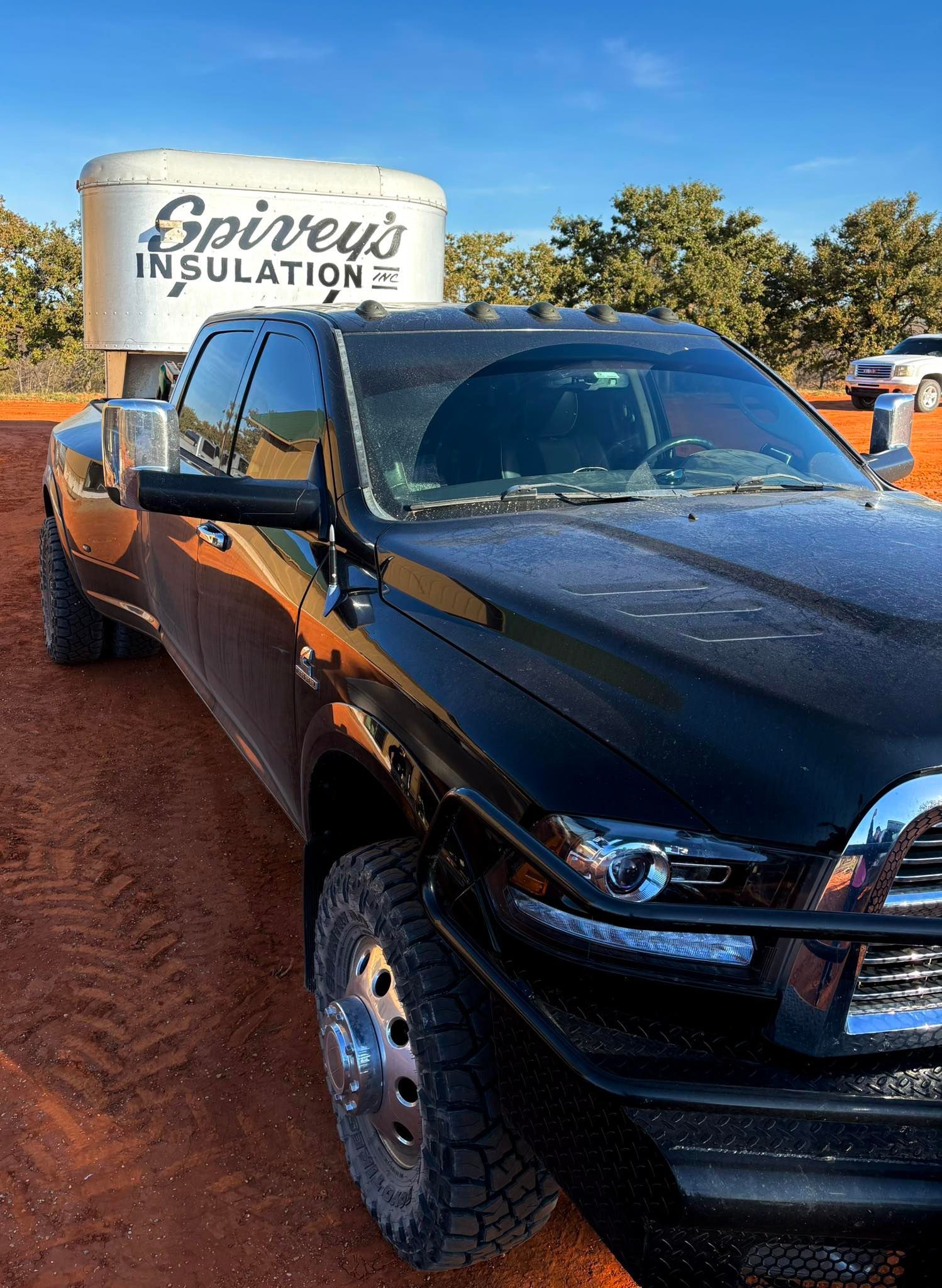 Black pickup truck parked on red dirt in front of a Spivey Insulation sign