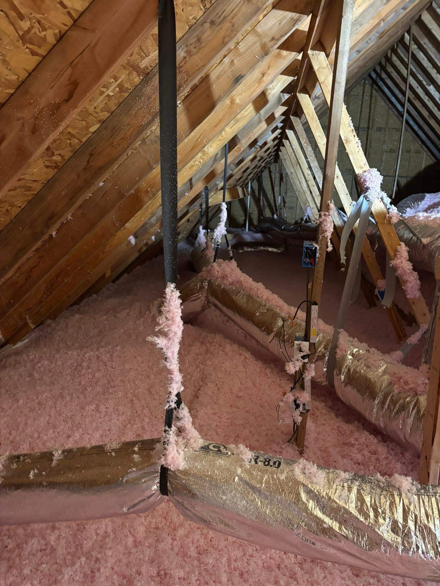 Attic interior with exposed wooden rafters, insulation, and a sloped ceiling around a central pole.