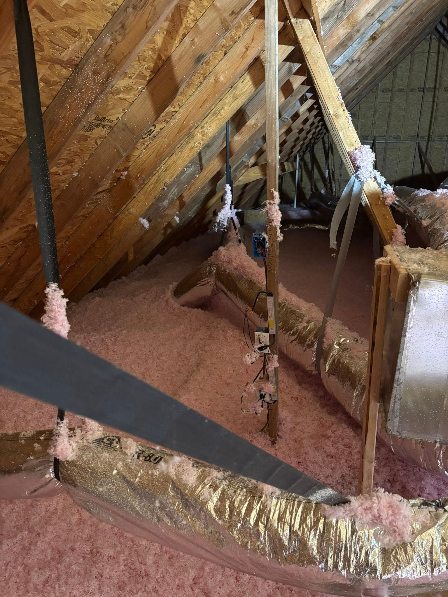 Attic with exposed wooden rafters, hanging ropes, and pink insulation under a sloped roof
