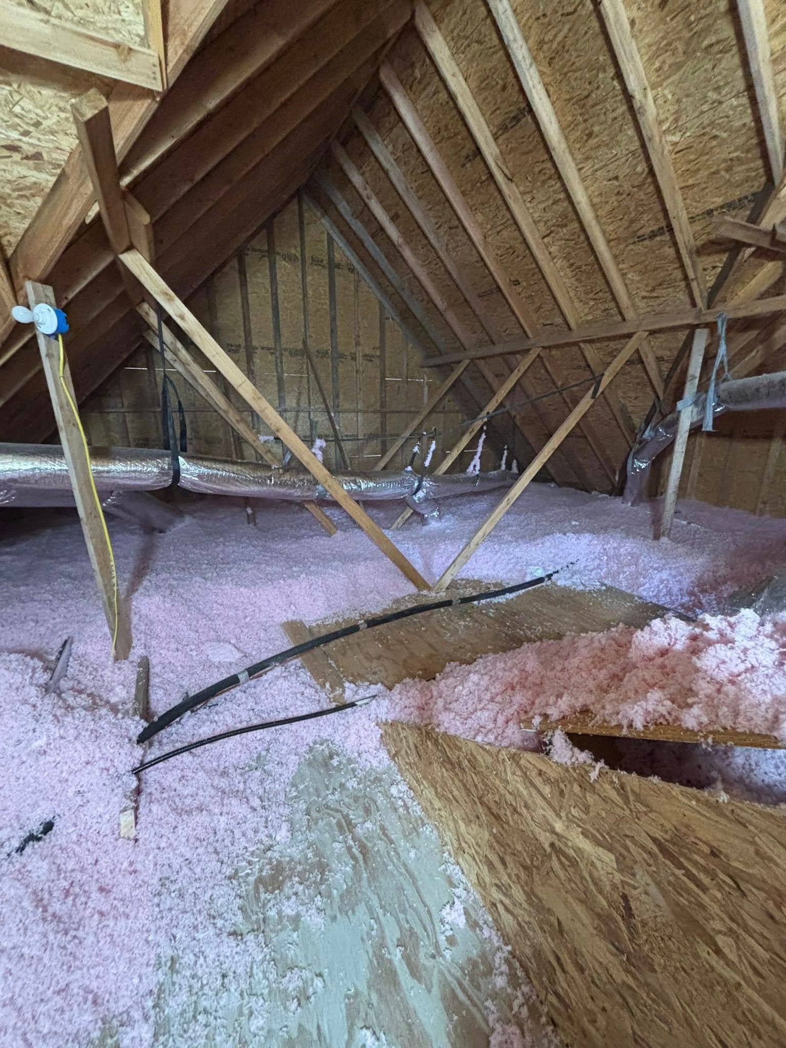 Attic with exposed wooden rafters, insulation, and a blue pipe amid scattered debris