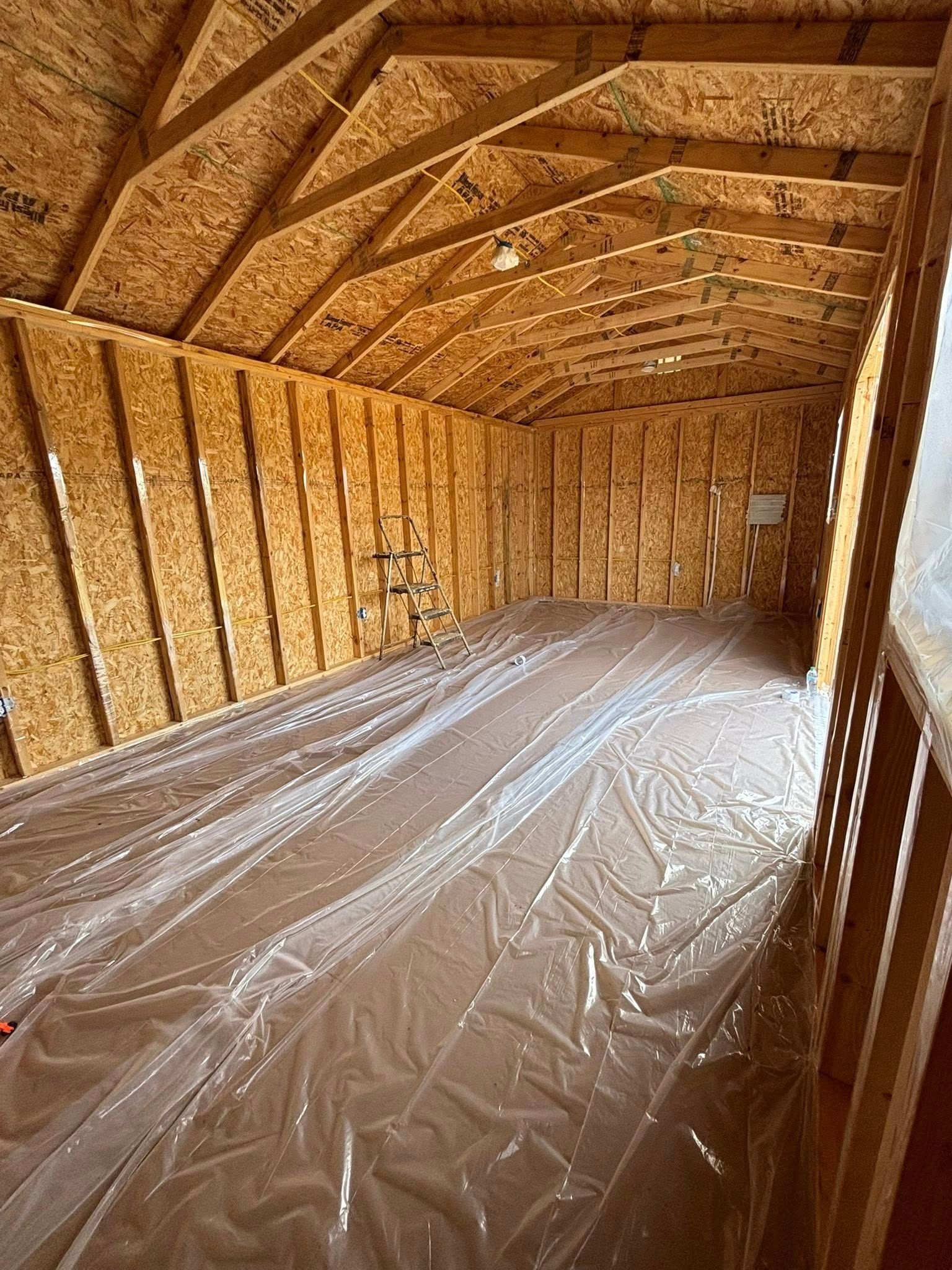 Interior of an unfinished wooden shed with exposed studs, slanted roof, and plastic-covered floor