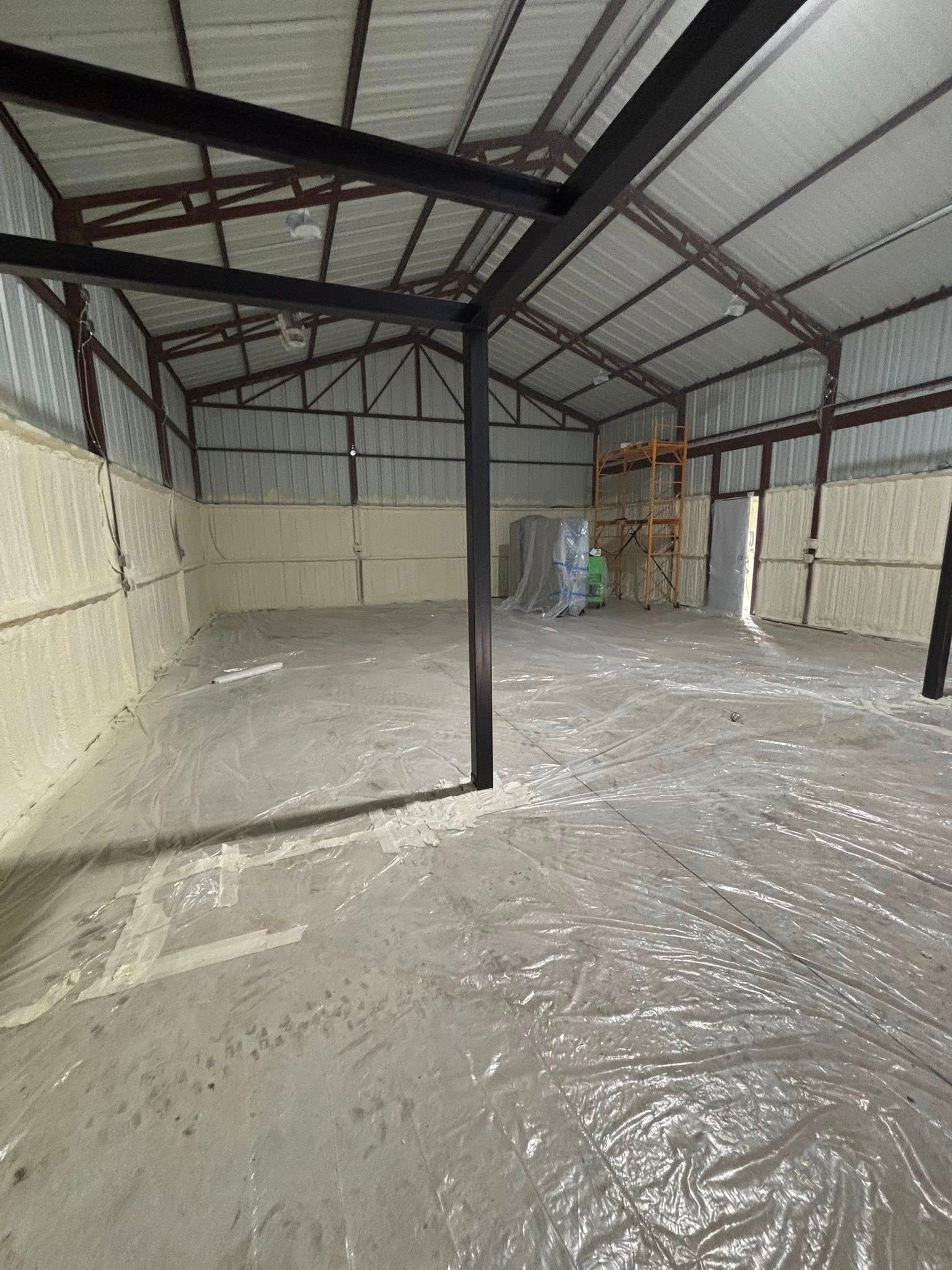 Empty warehouse with metal roof, white walls, and plastic-covered floor under construction.