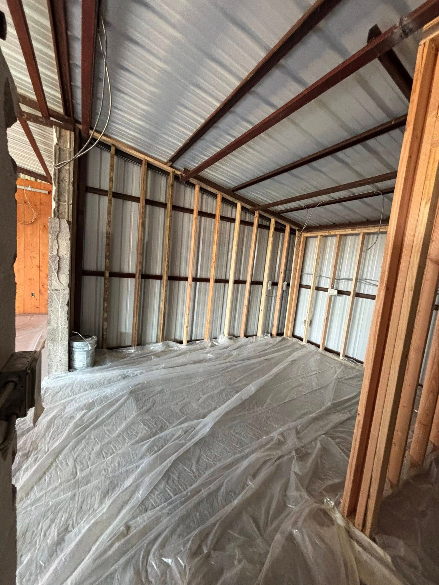 Unfinished room with exposed framing, corrugated metal ceiling, and plastic sheeting on the floor.