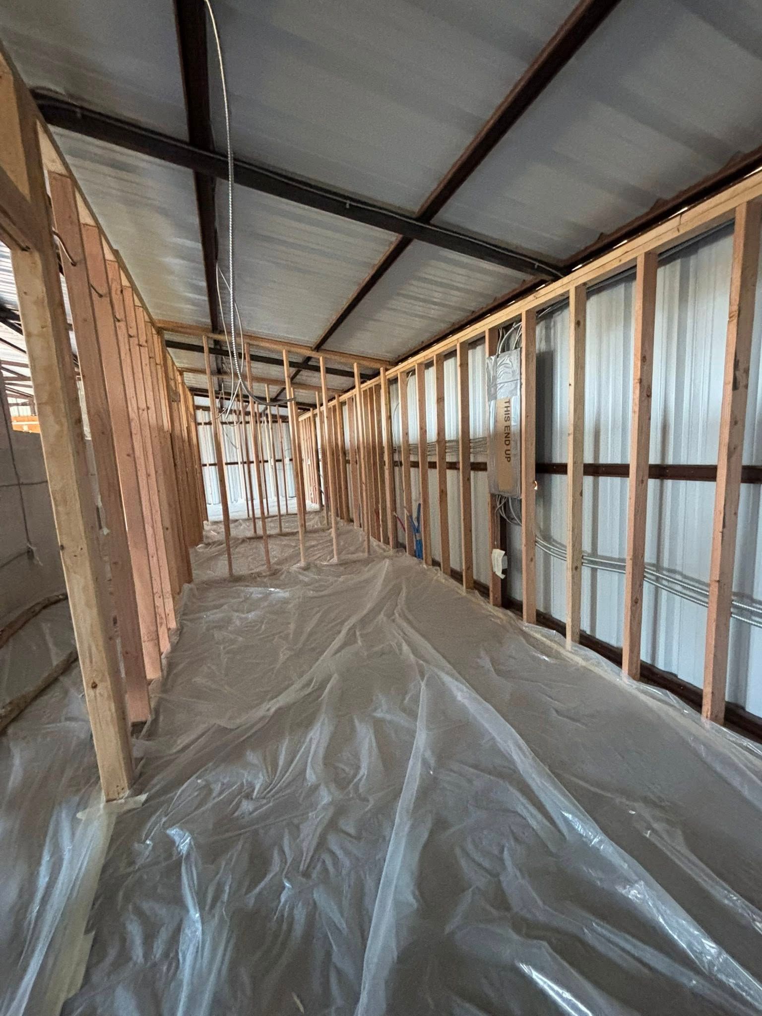 Unfinished attic with exposed wooden framing, insulation, and plastic sheeting on the floor