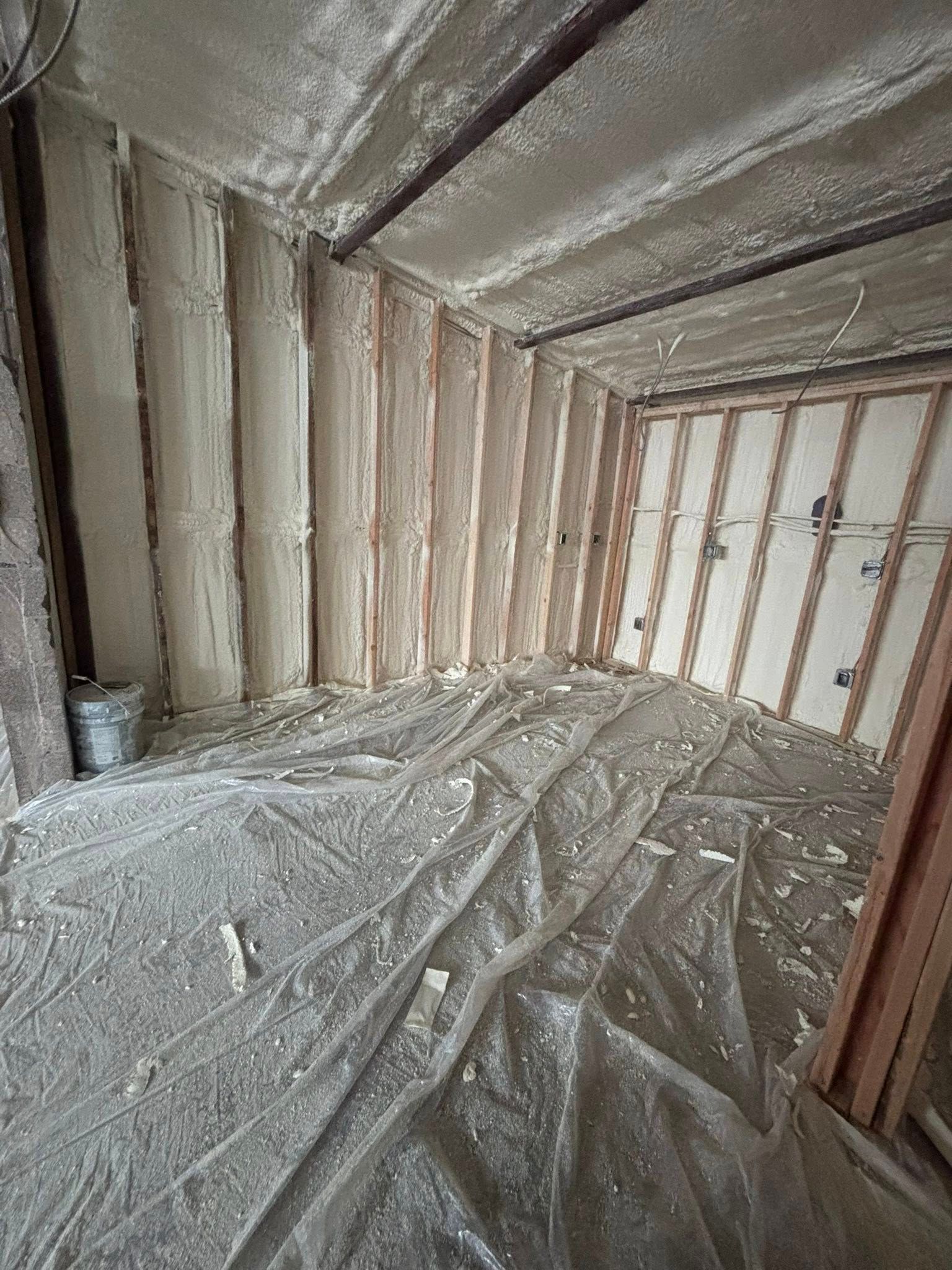 Insulated attic interior with exposed framing and plastic sheeting on the floor