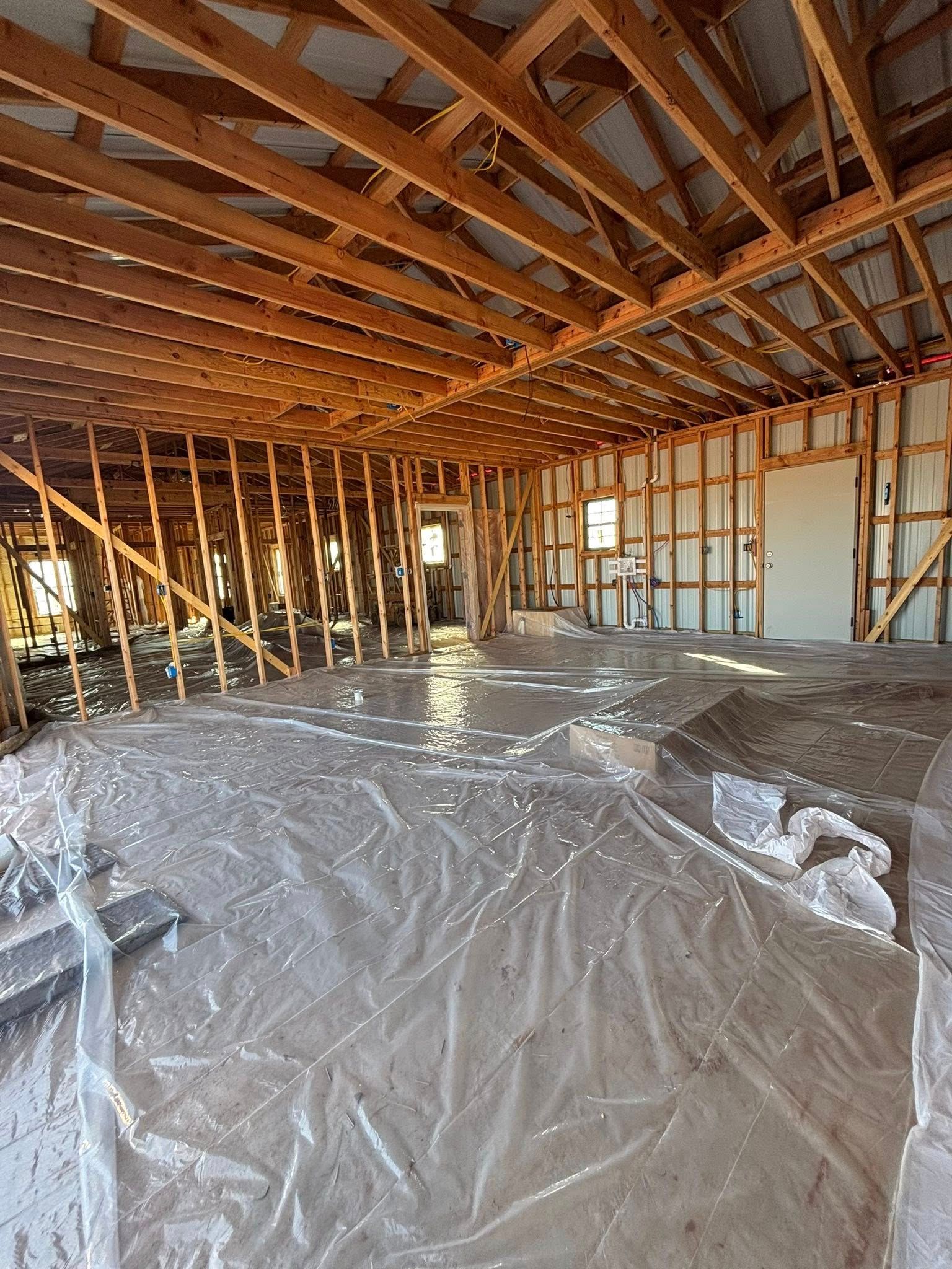 Unfinished house interior with exposed wooden framing and plastic-covered floor.