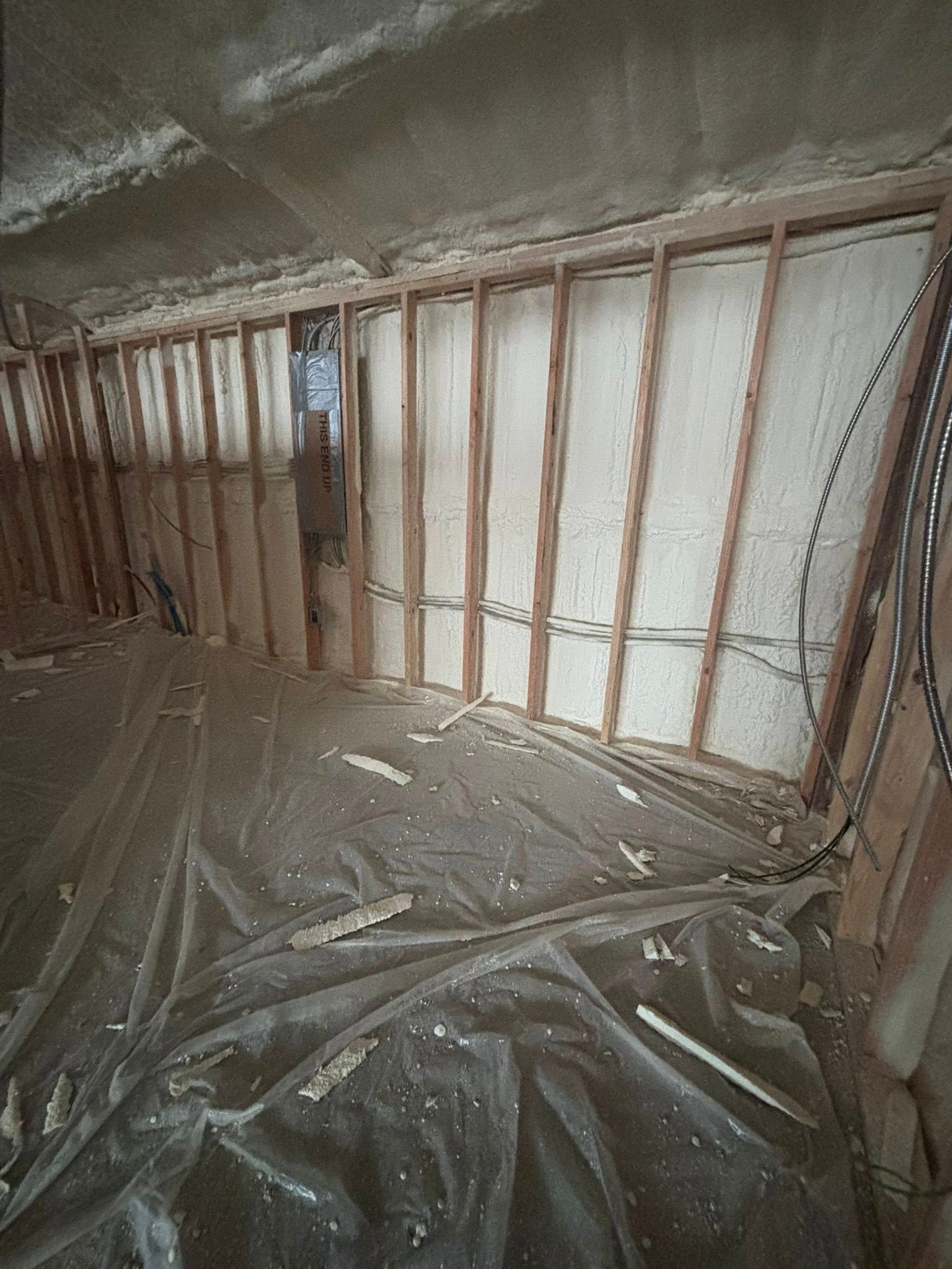 Insulated attic with exposed wooden framing and plastic sheeting covering the floor and walls.