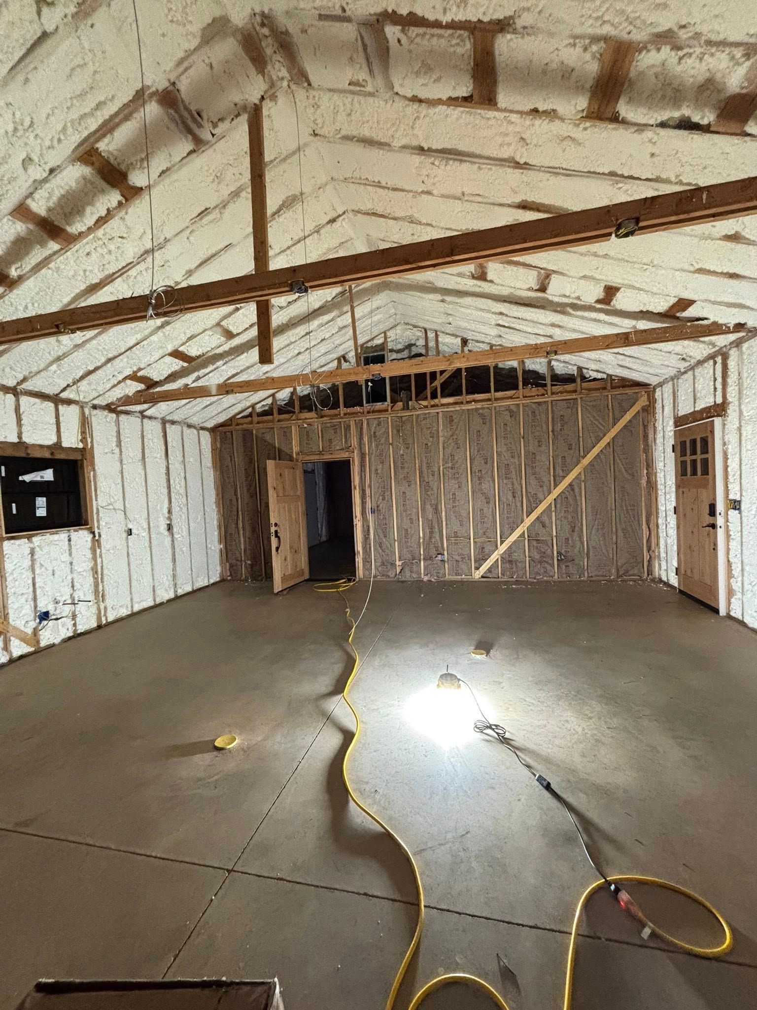 Empty unfinished interior with exposed beams, white walls, concrete floor, and a cord on the ground.
