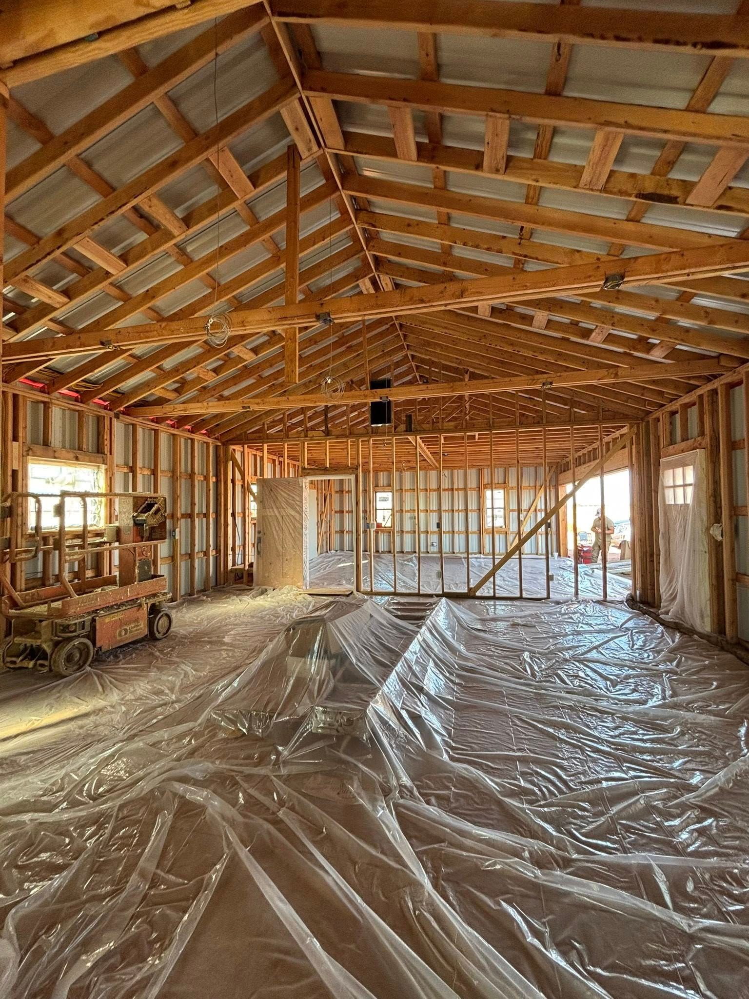 Unfinished house interior with exposed wooden rafters and plastic-covered floor during construction.