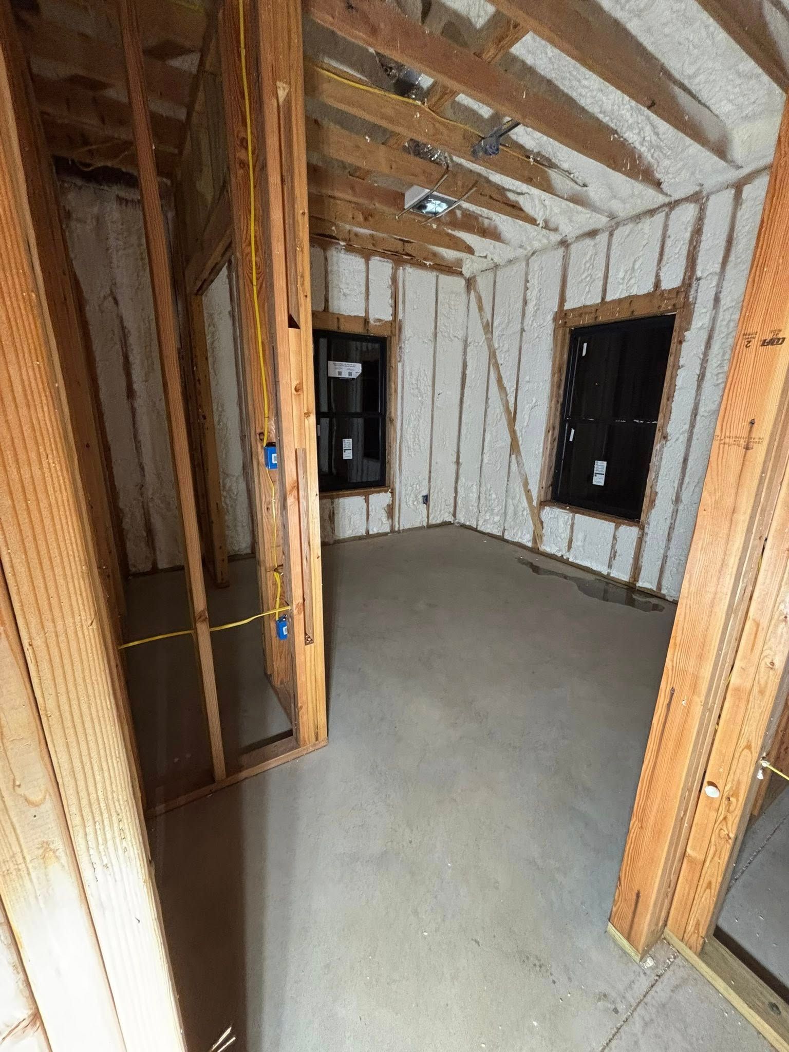 Interior of a stripped room with exposed wooden framing, insulation, and a concrete floor.